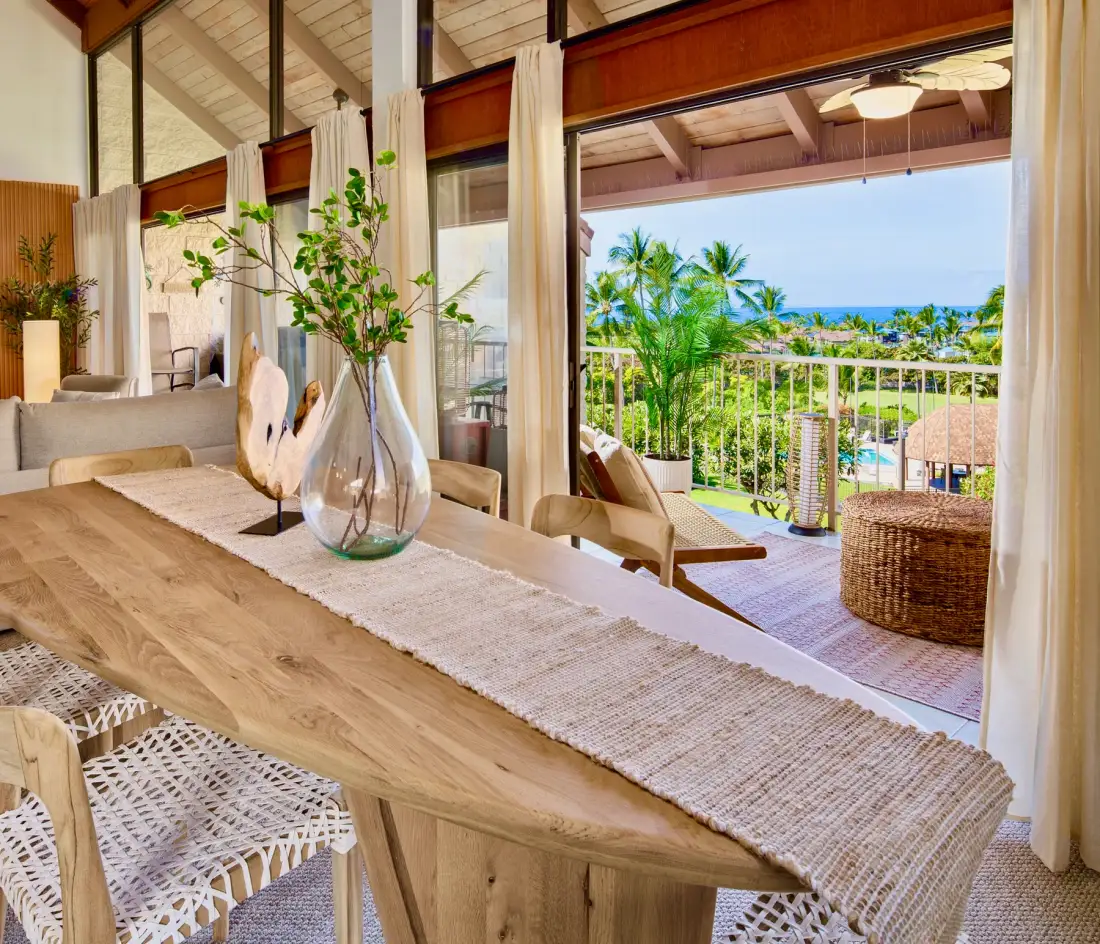 A dining area opens through wide glass doors onto a balcony with tropical greenery.