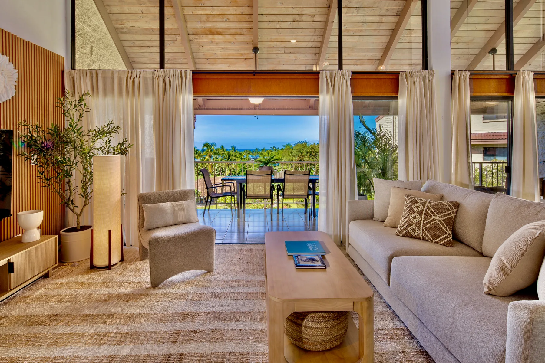A bright living room opens onto a patio with seating and greenery.