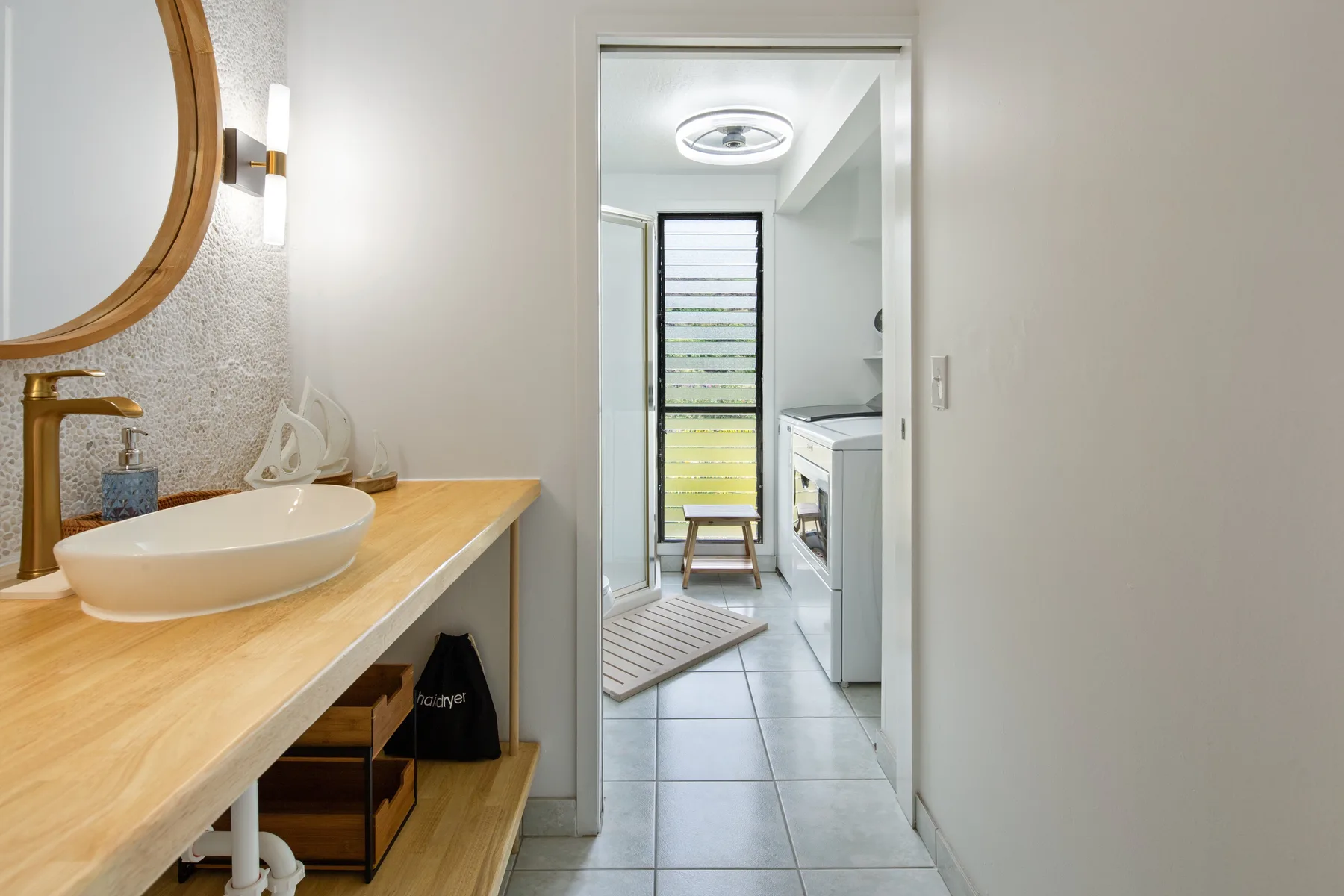 A bathroom vanity with a vessel sink opens onto a bright laundry area.