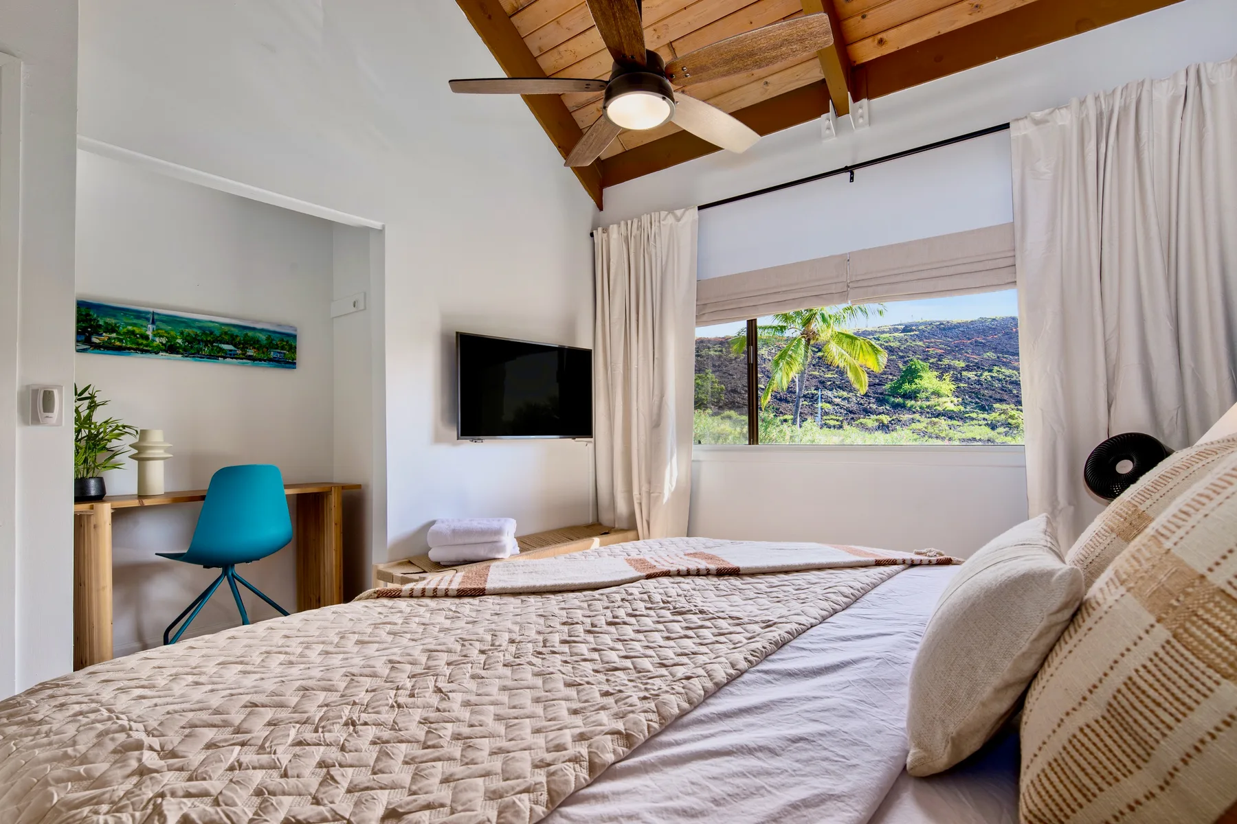 A bedroom with a bed, a desk, and a wide window overlooking greenery.