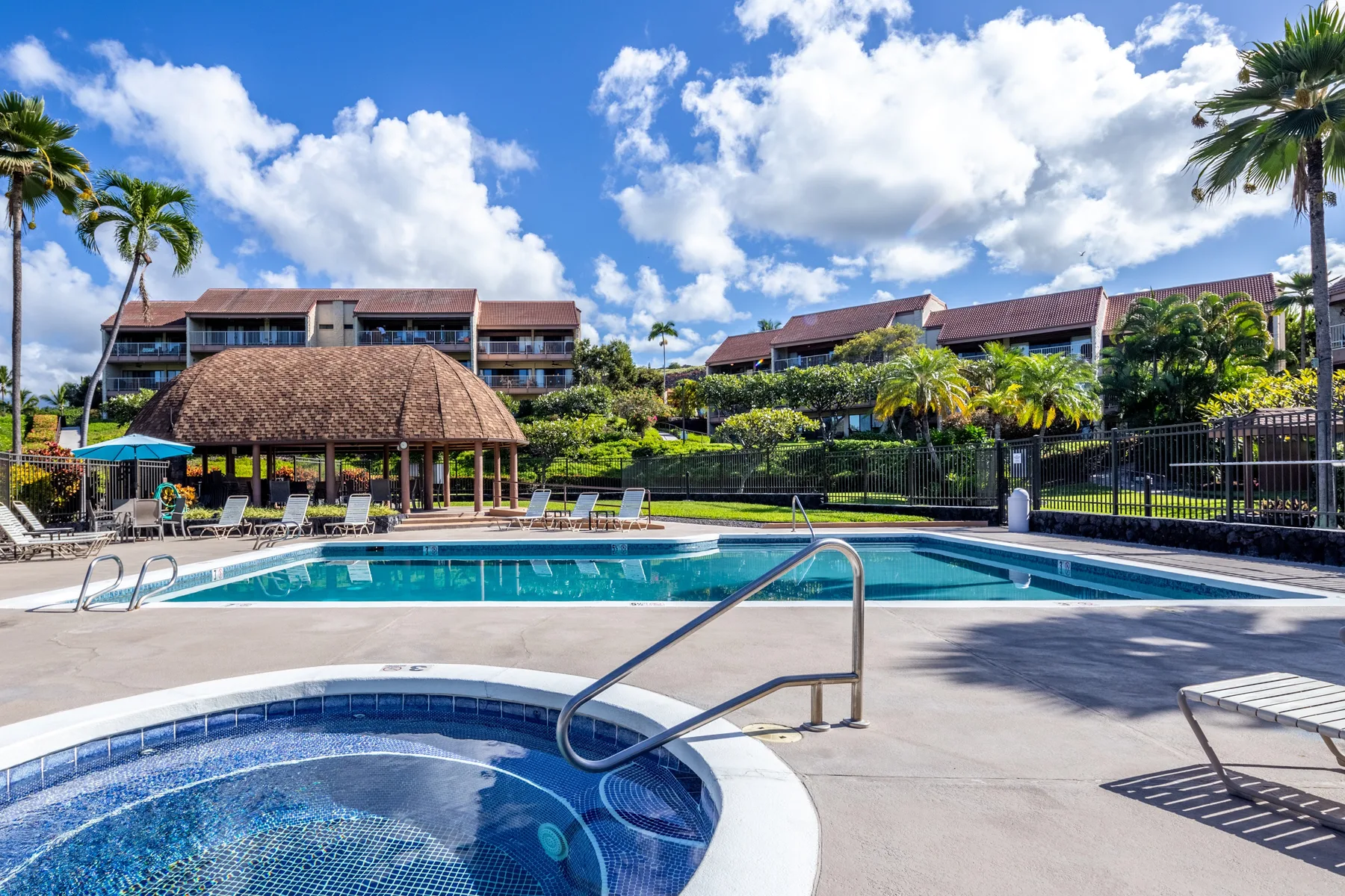 An outdoor swimming pool and spa sit beside a thatched-roof pavilion.
