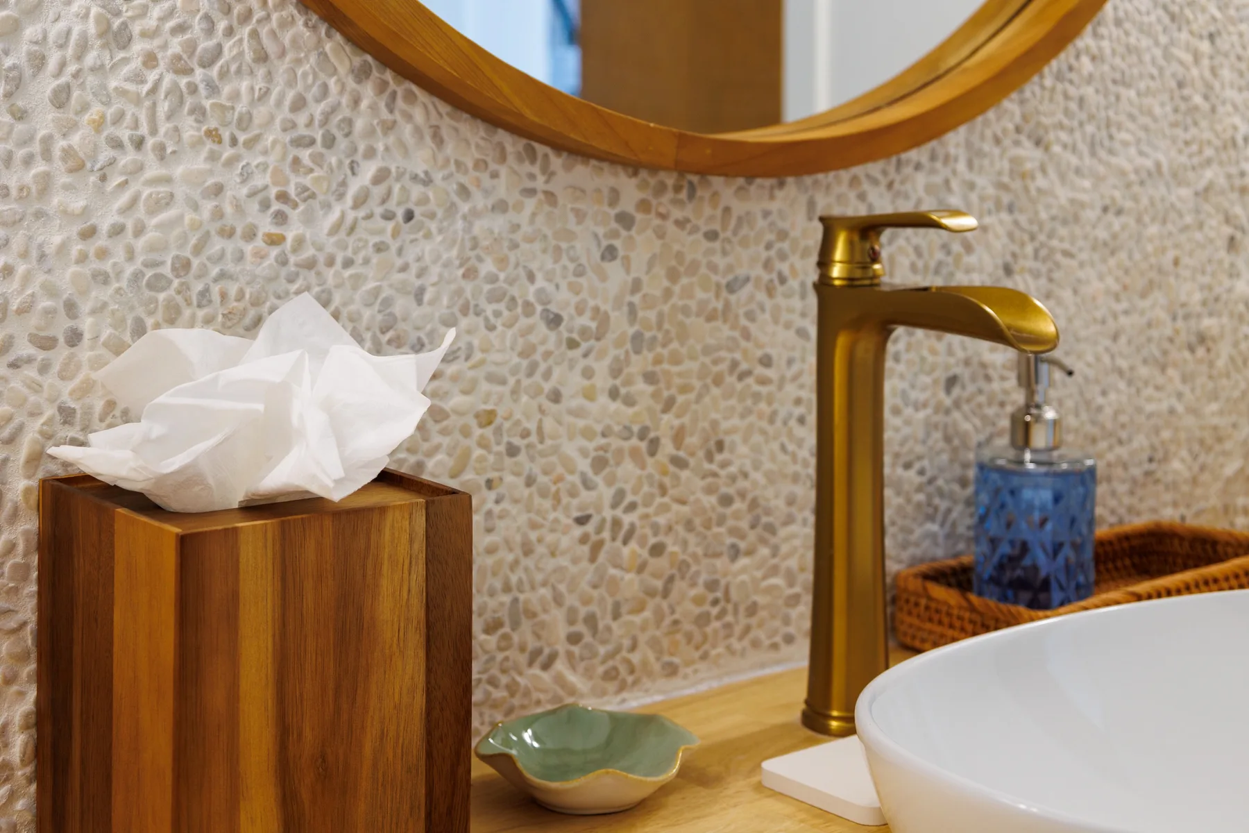 A bathroom vanity with a gold faucet, white basin, and pebble-patterned wall.