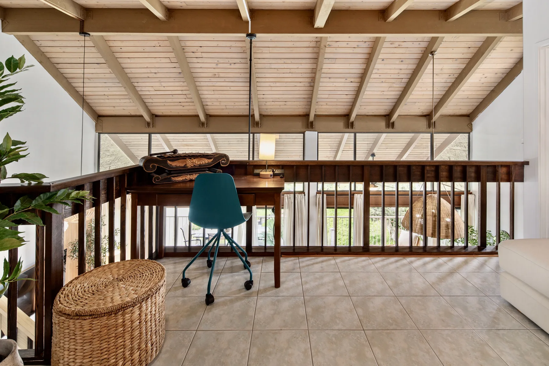 A bright loft sitting area with a desk, seating, and exposed timber beams.