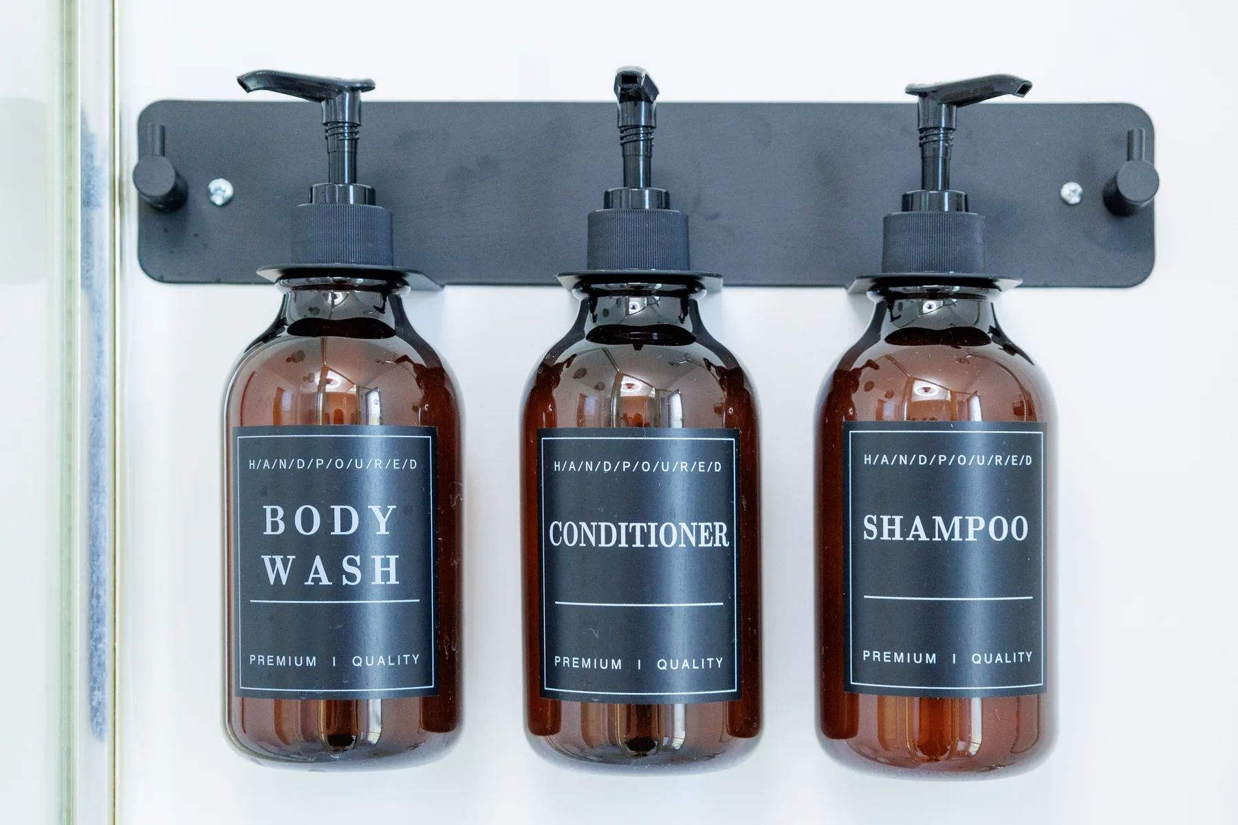 A wall-mounted bathroom dispenser holds bottles of body wash, conditioner, and shampoo.