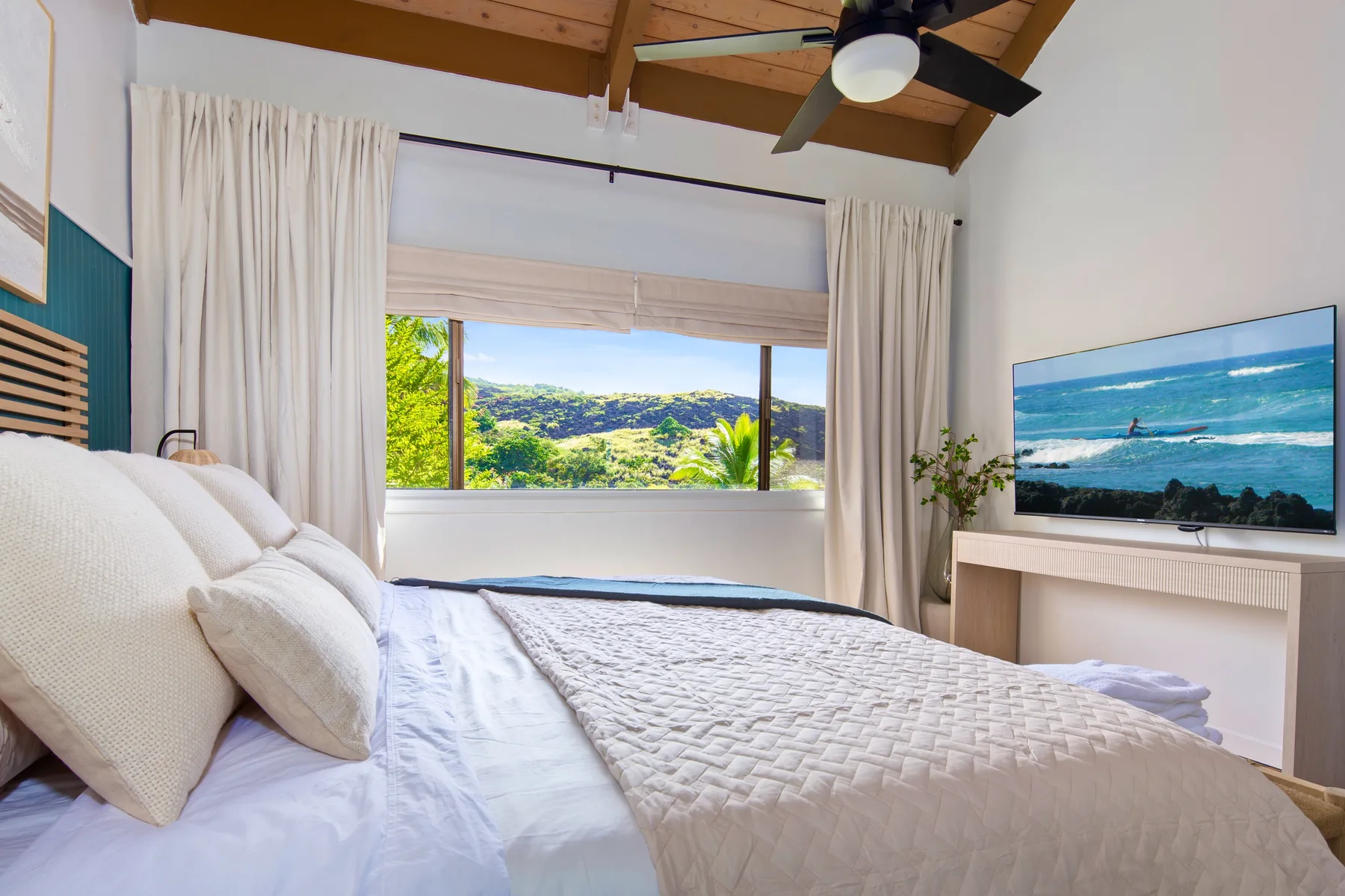 A bedroom with a bed facing a wide window overlooking green hills.