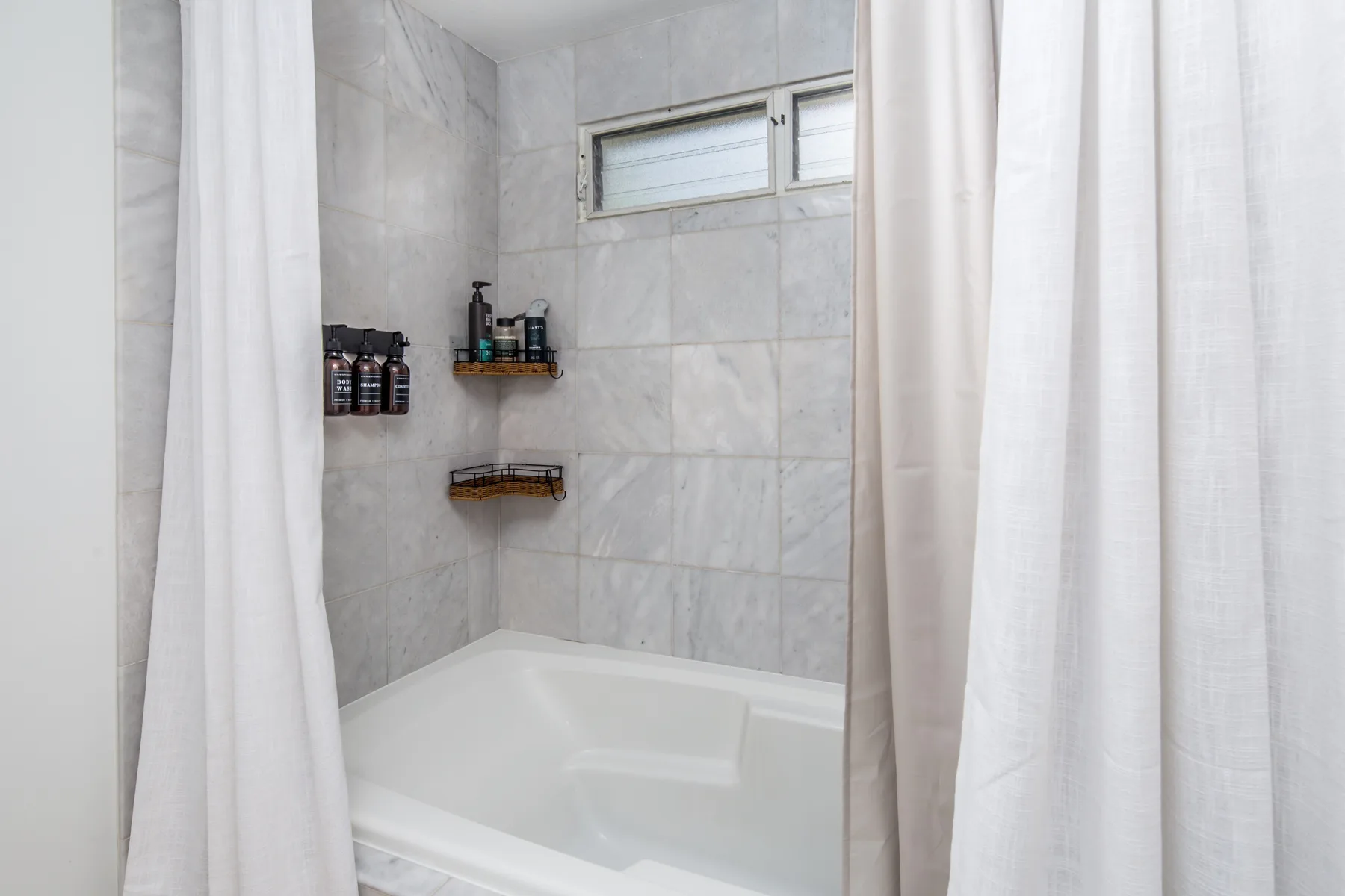A tiled bathroom with a bathtub and a small high window.