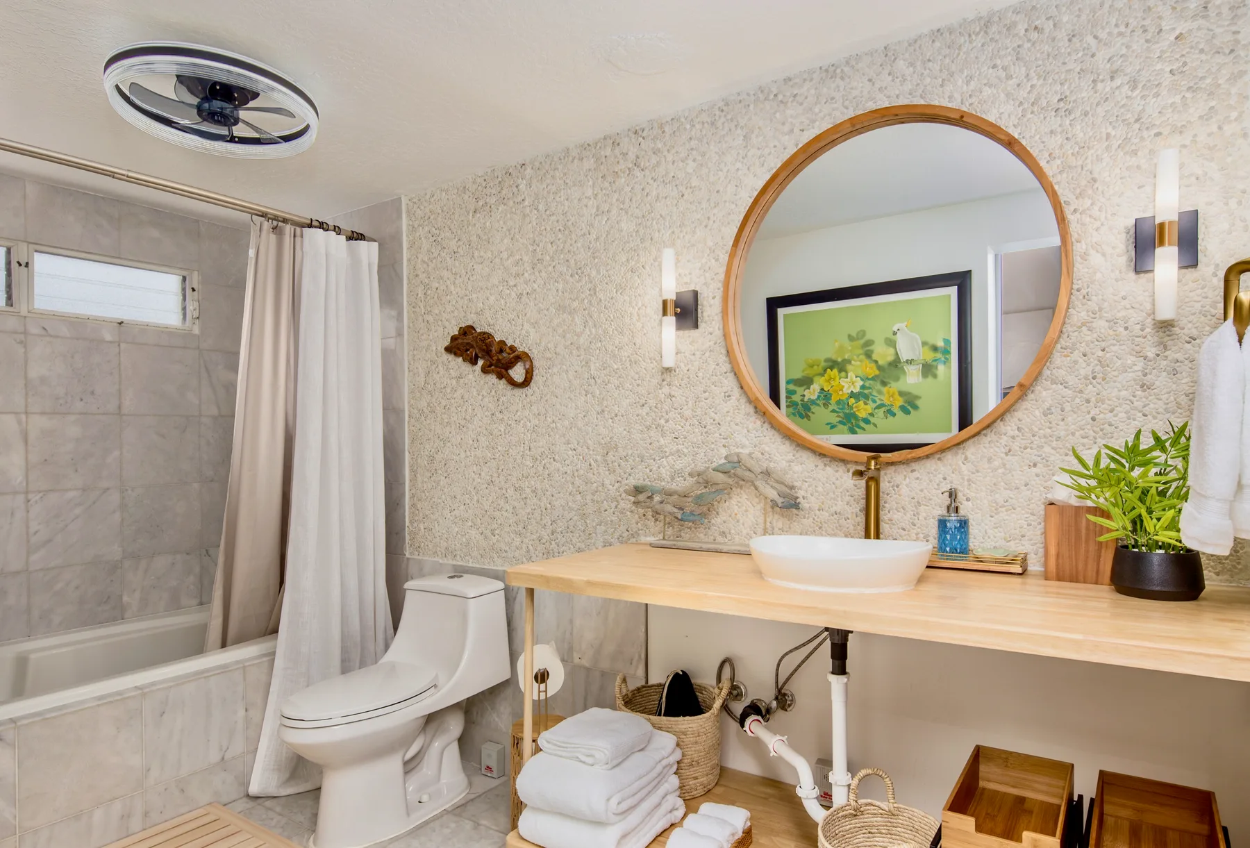 A bathroom with a bathtub, toilet, and vanity topped by a round mirror.