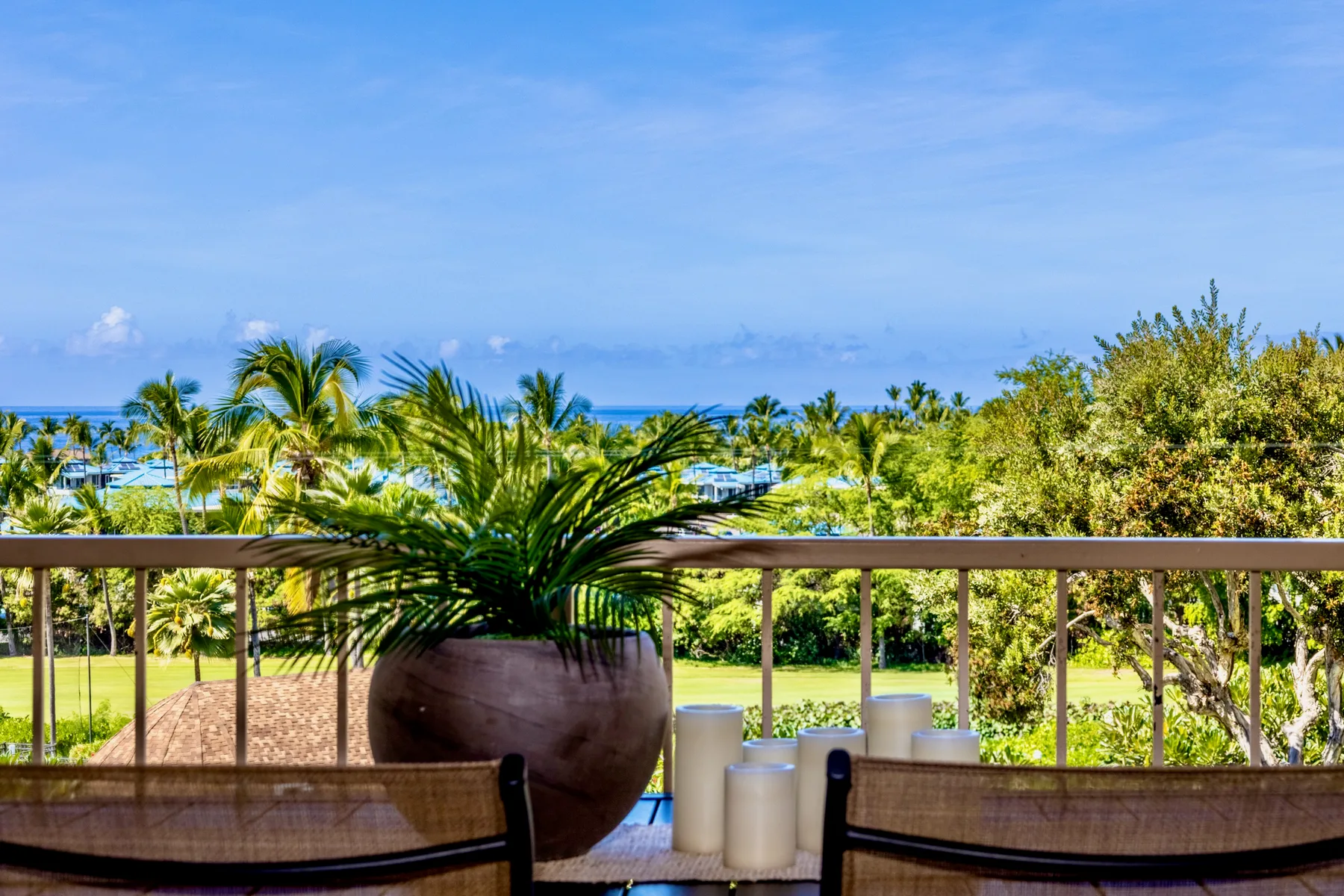 A balcony seating area overlooks palm trees and the ocean.