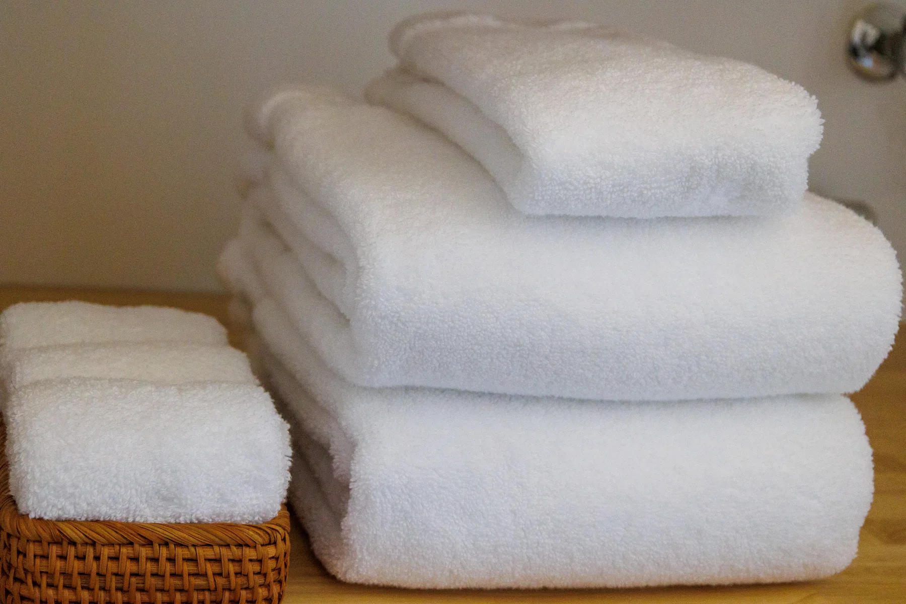 Folded white towels are stacked on a wooden surface beside a woven basket.