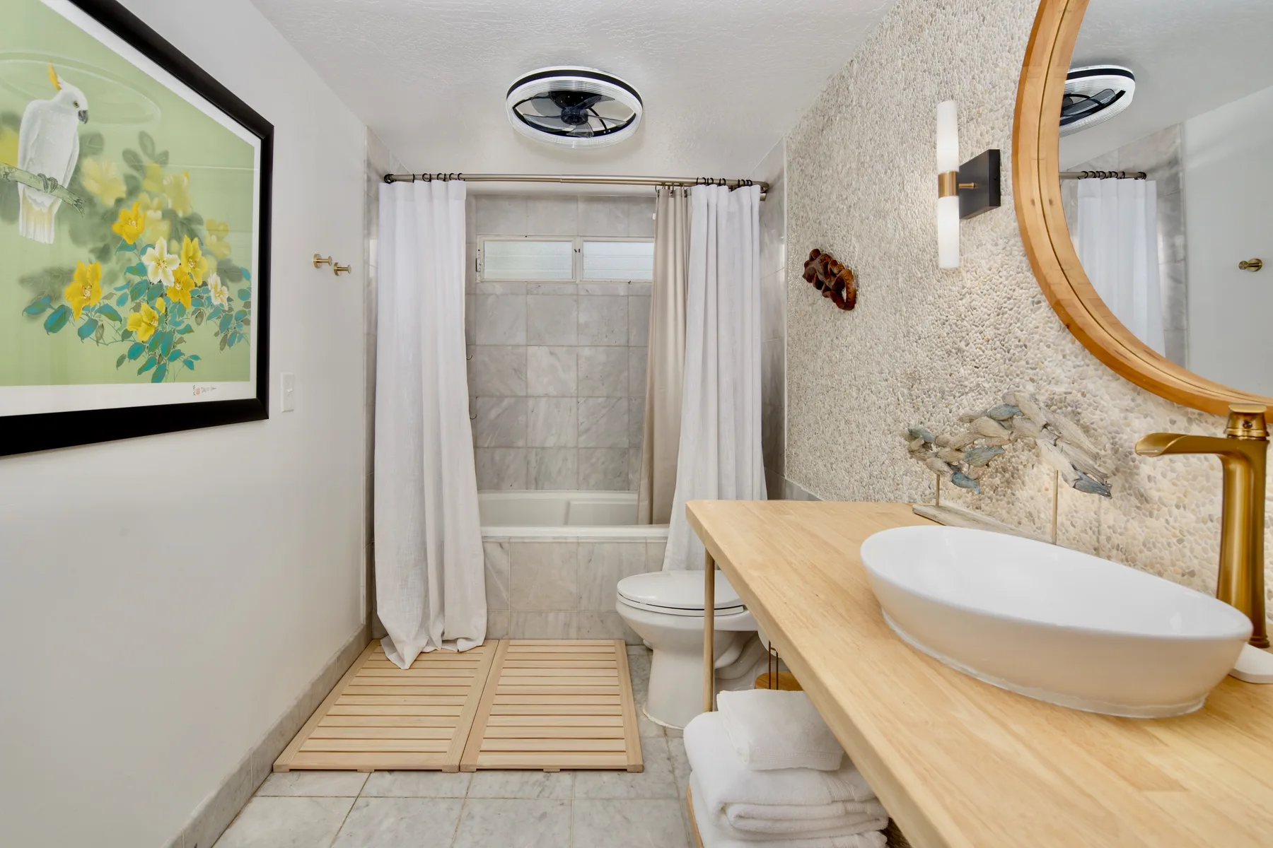 A bathroom with a bathtub, toilet, and sink beneath a round mirror.