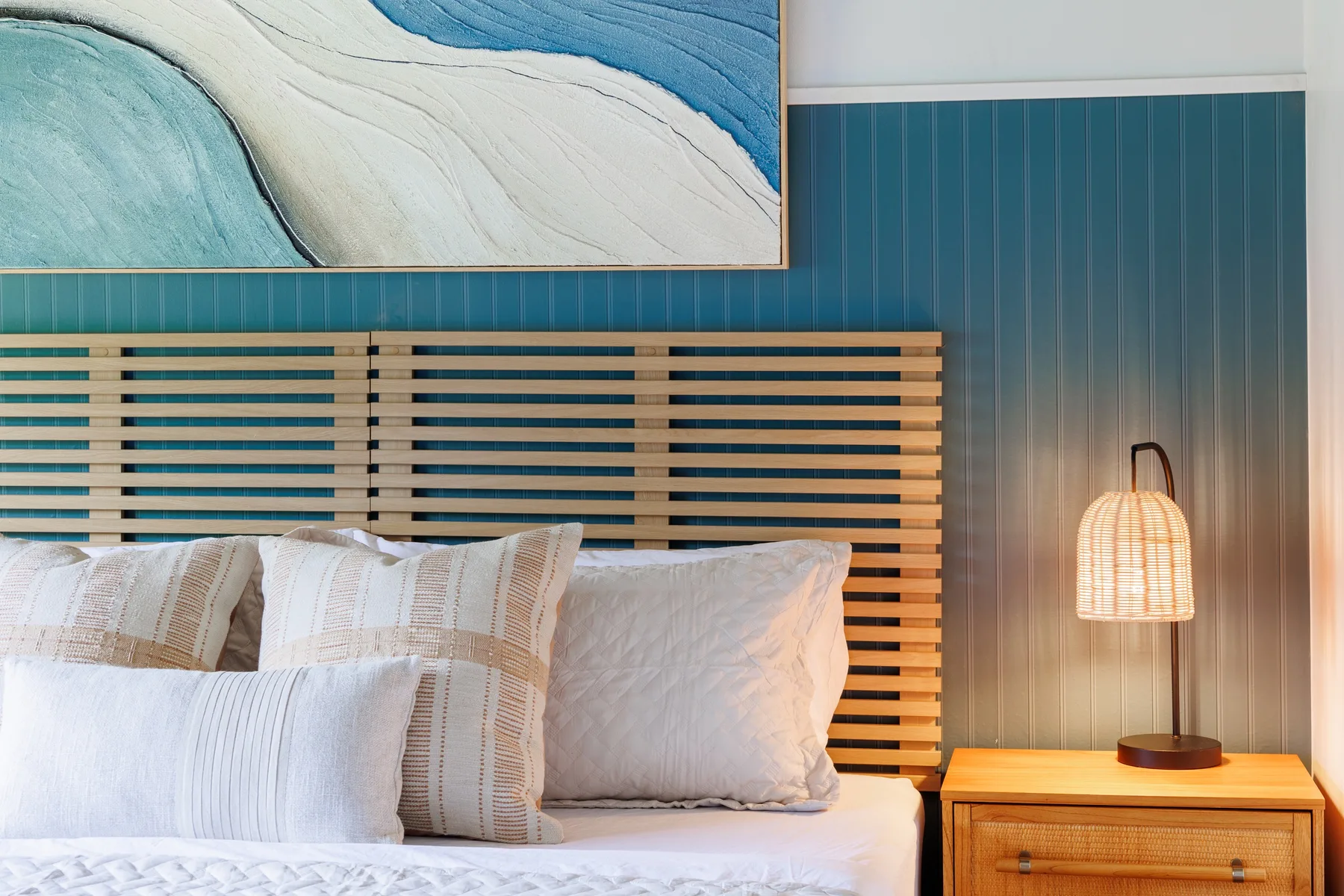 A bedroom with a bed against a teal paneled wall and a bedside lamp.