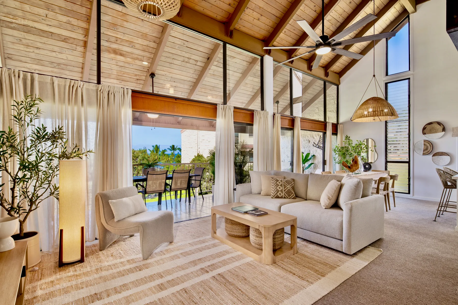 A bright living room opens onto a patio, with seating beneath a high wooden ceiling.