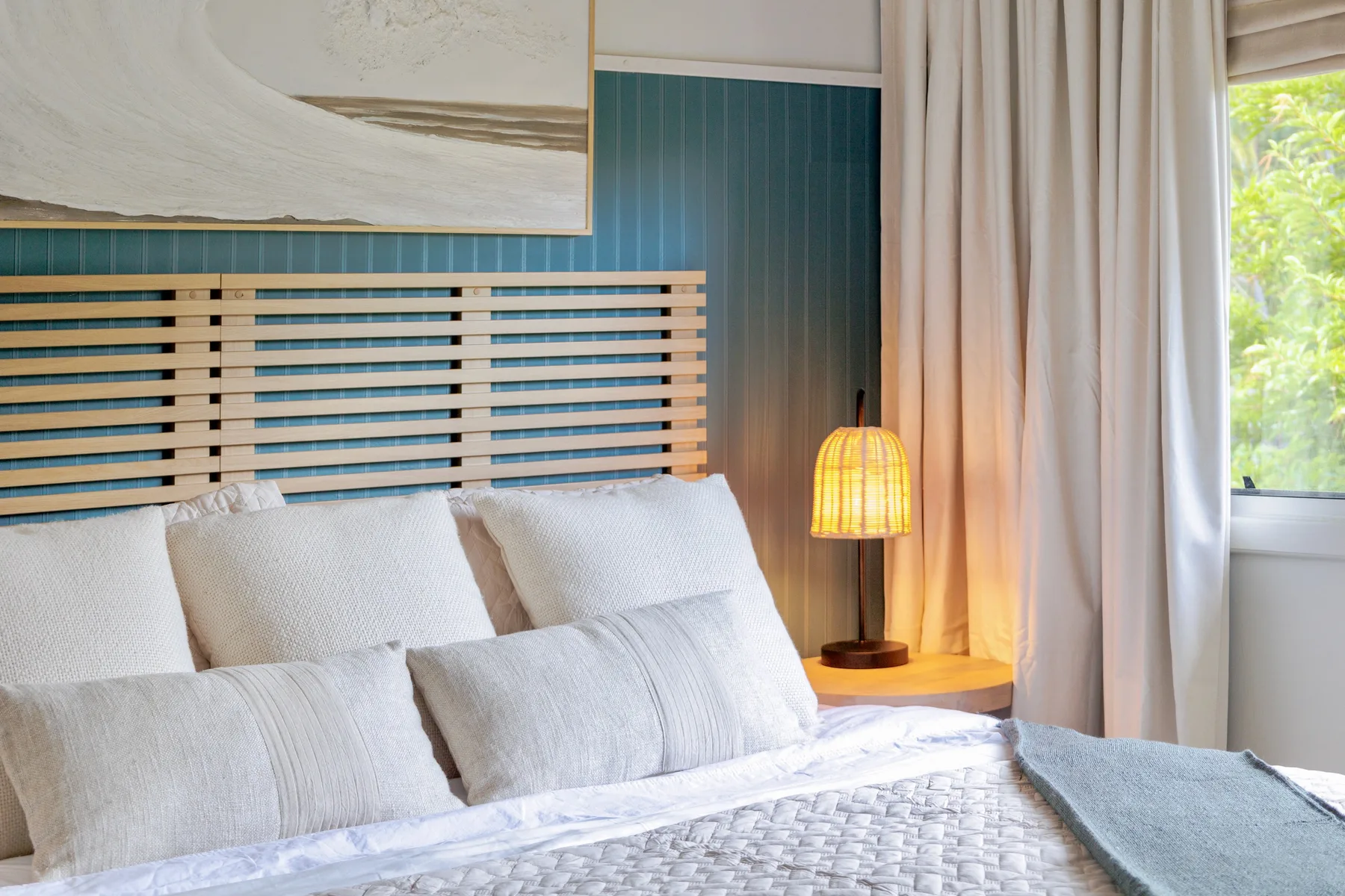 A bedroom with a bed, teal paneled wall, and a glowing bedside lamp.