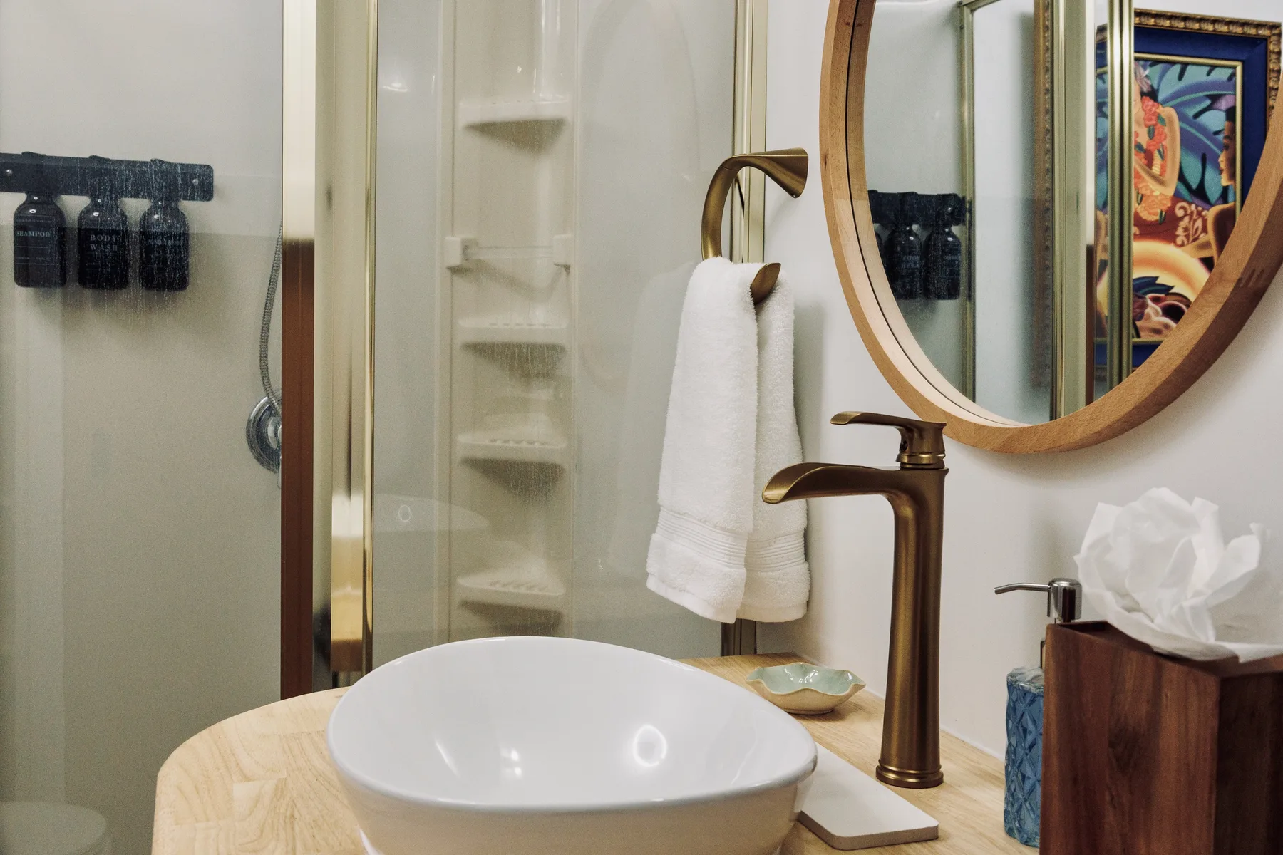 A bathroom vanity with a white basin, bronze faucet, and round mirror.