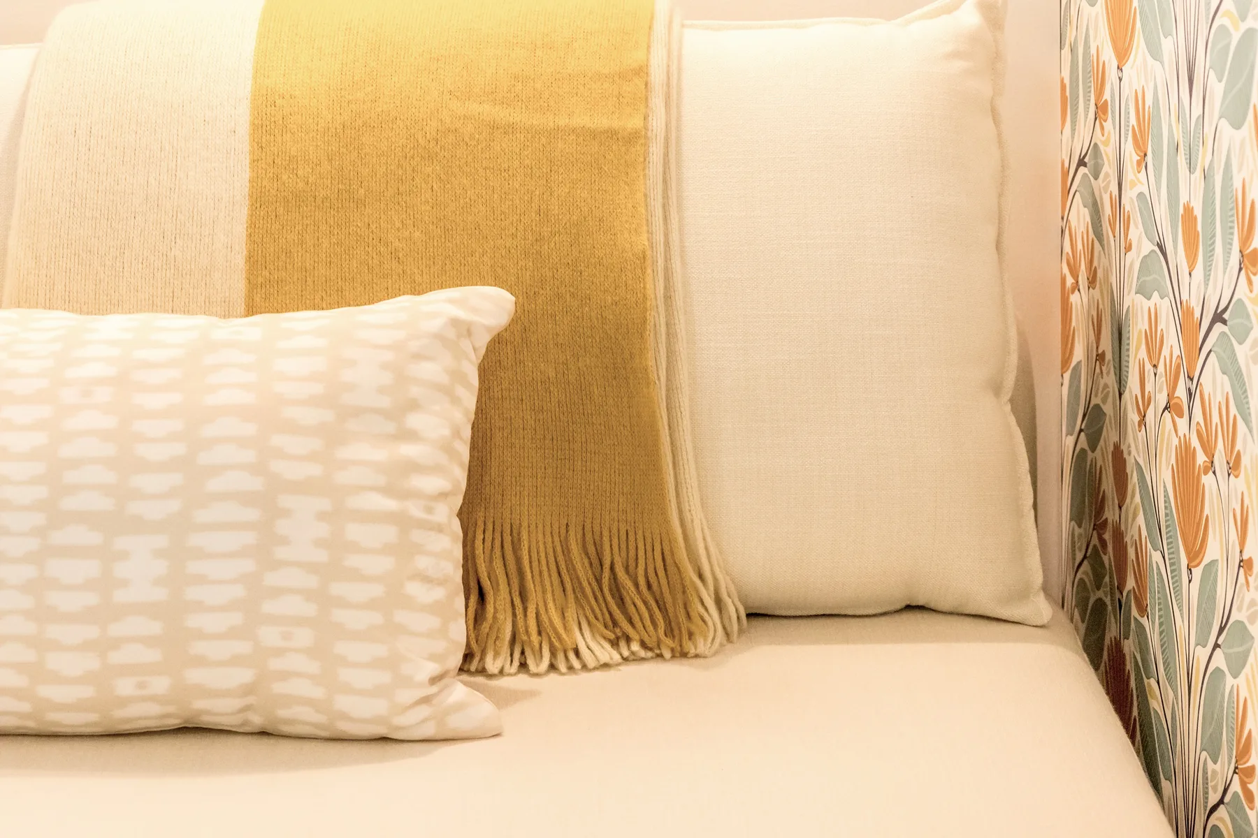 A bed with patterned pillows and a golden throw beside floral curtains.