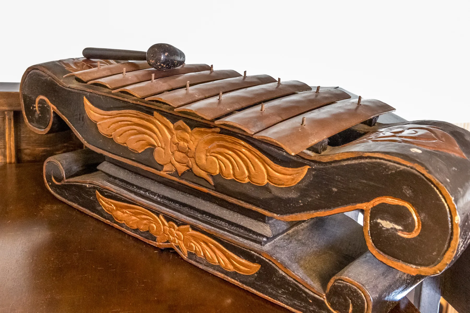 A carved wooden musical instrument rests on a polished wooden surface.