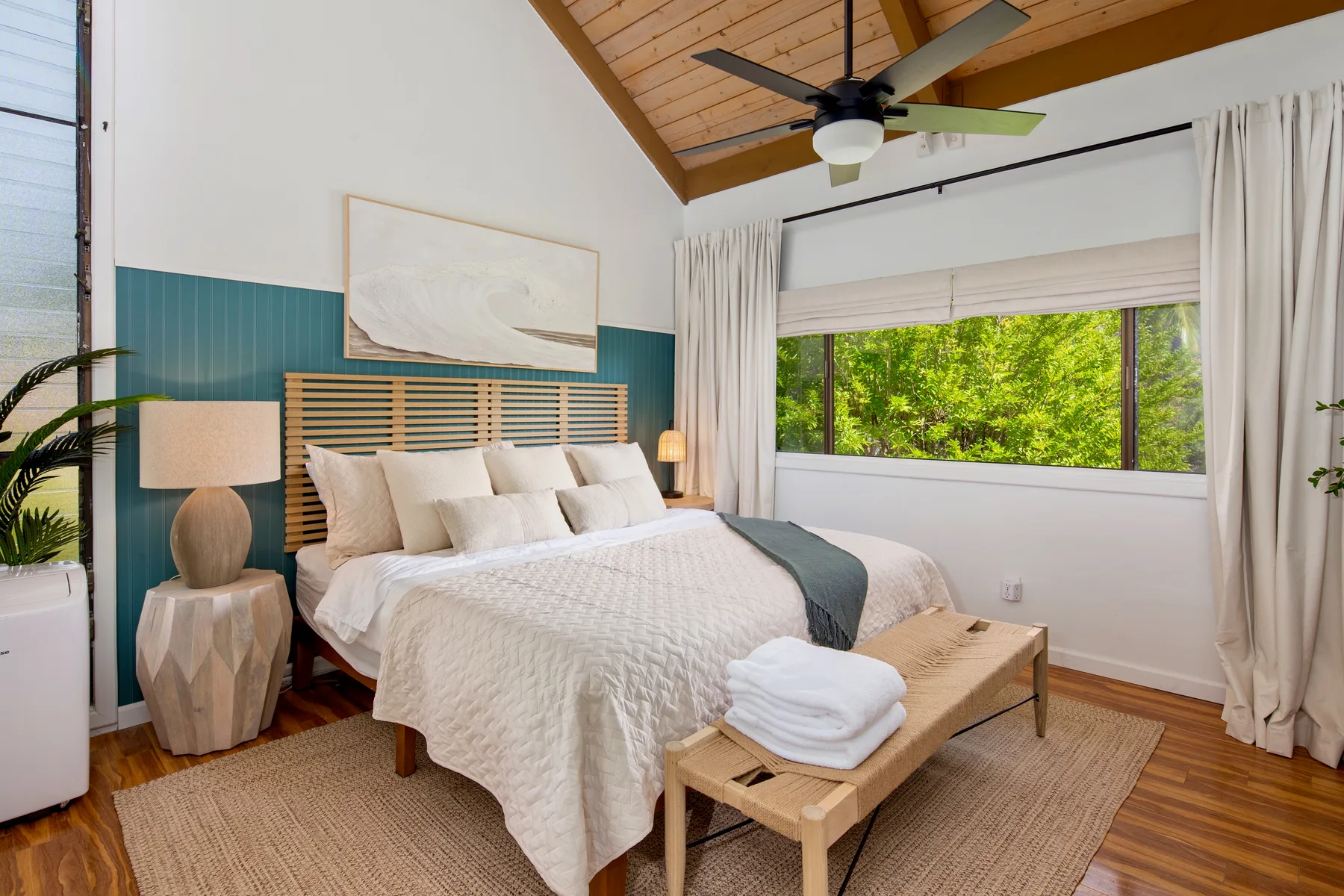 A bright bedroom with a large bed and a wide window overlooking greenery.