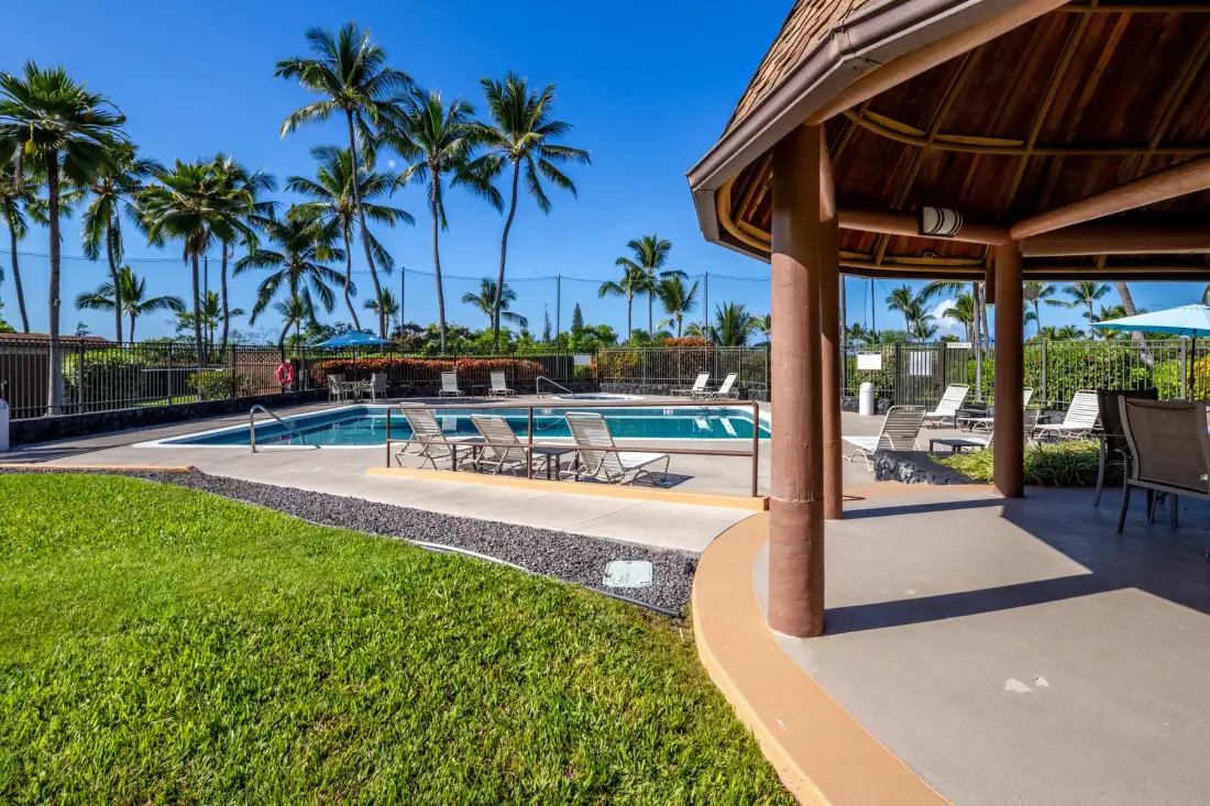 An outdoor swimming pool beside a covered patio with lounge seating.