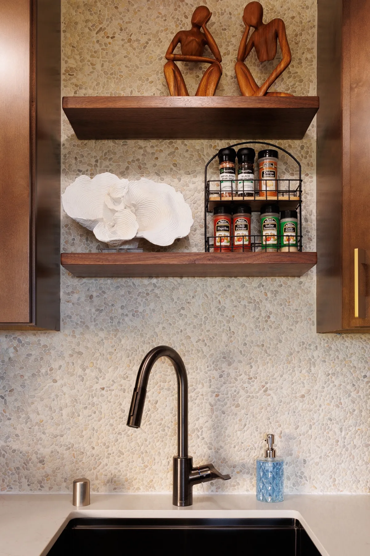 A kitchen sink beneath open shelves holding spice jars and decorative sculptures.