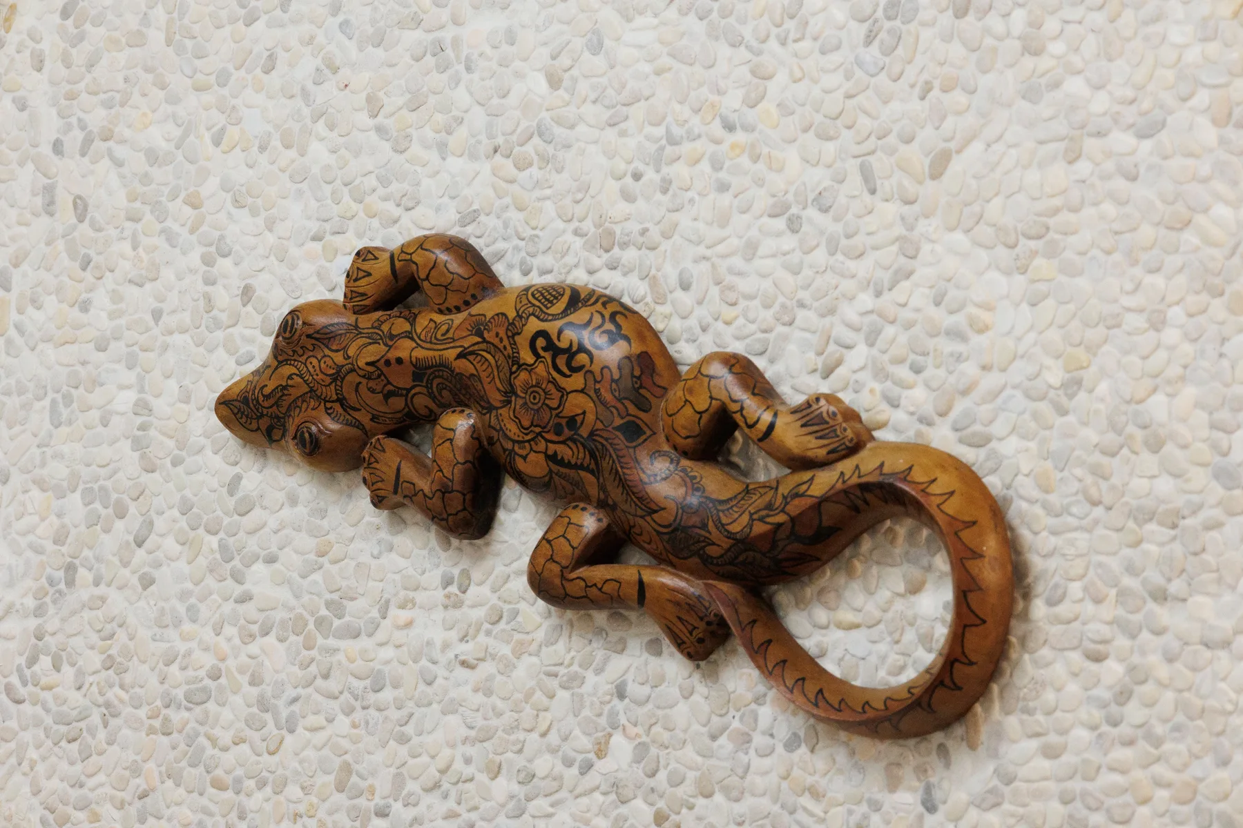 A carved wooden lizard with dark decorative patterns rests on a pale textured surface.