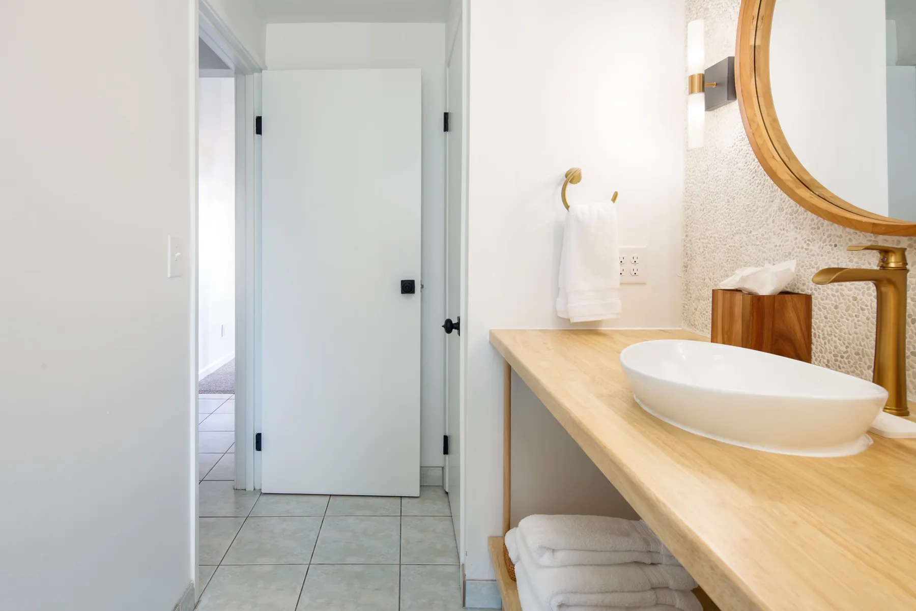 A bright bathroom with a long vanity, vessel sink, and round mirror.