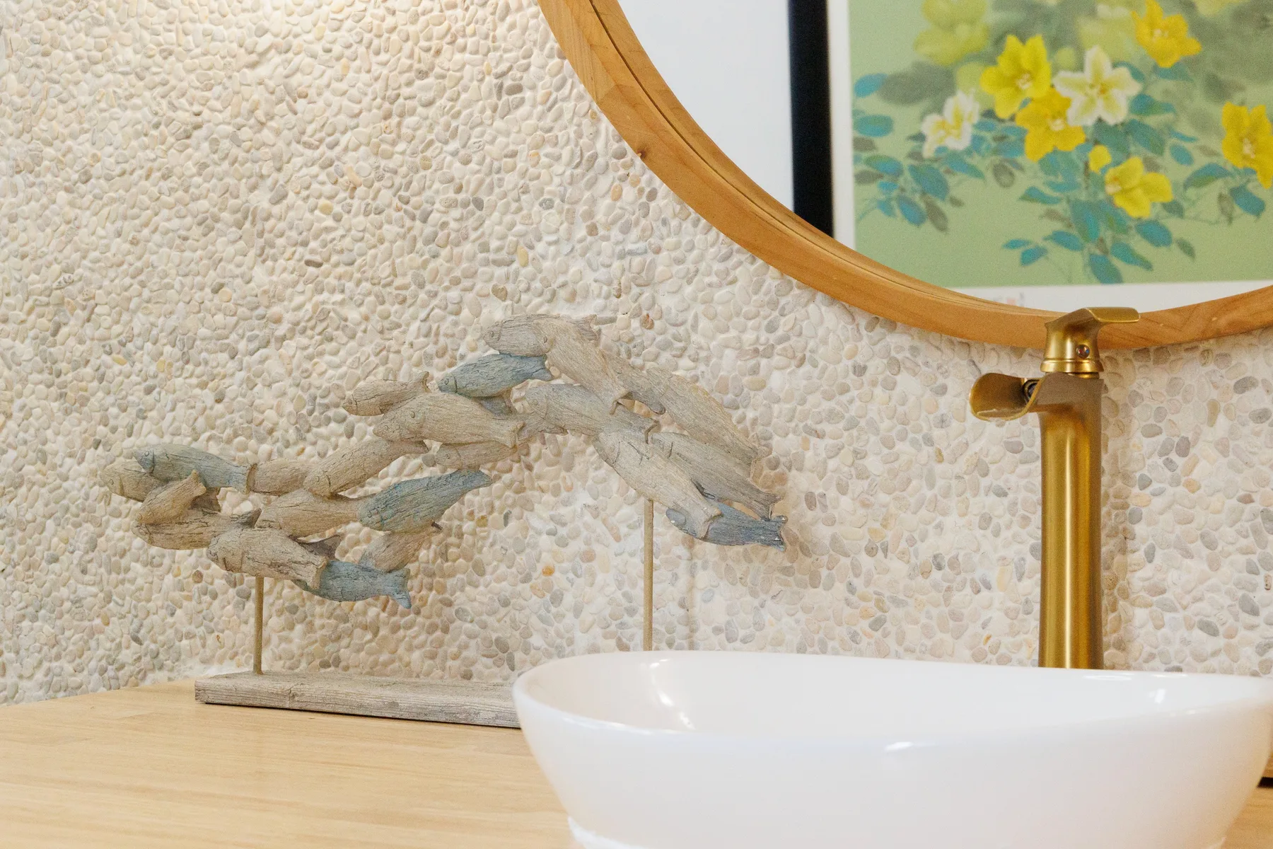 A bathroom vanity with a white vessel sink, round mirror, and decorative wall art.