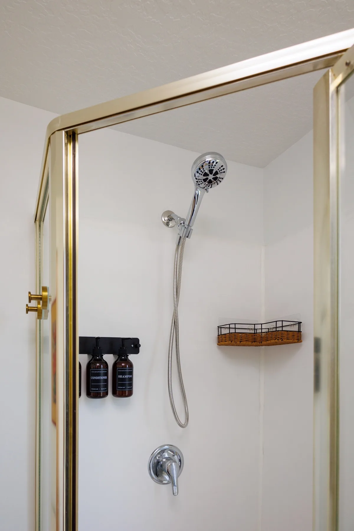 A shower with a handheld showerhead and wall-mounted basket.