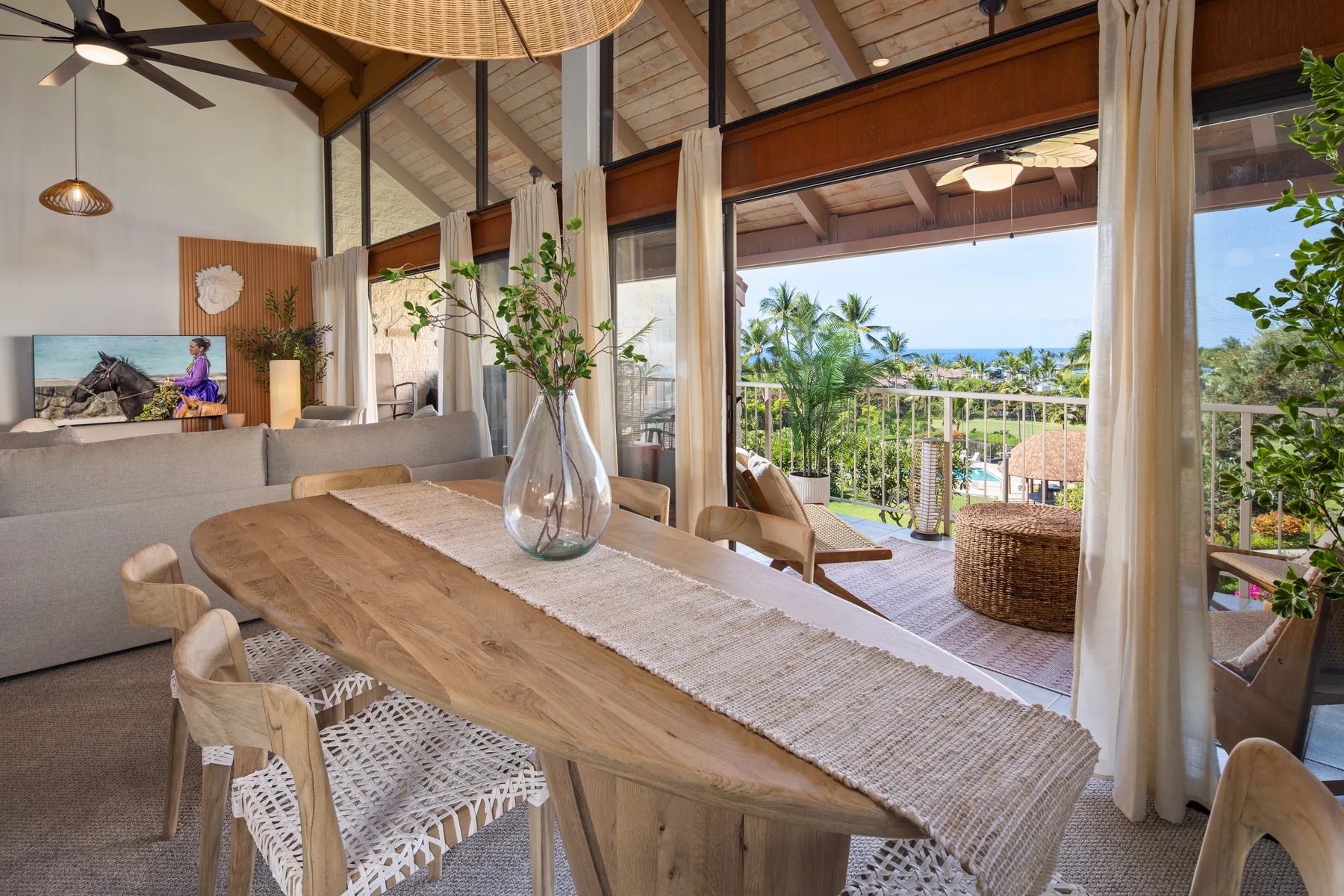 A dining area opens onto a balcony with tropical greenery and a sea view.