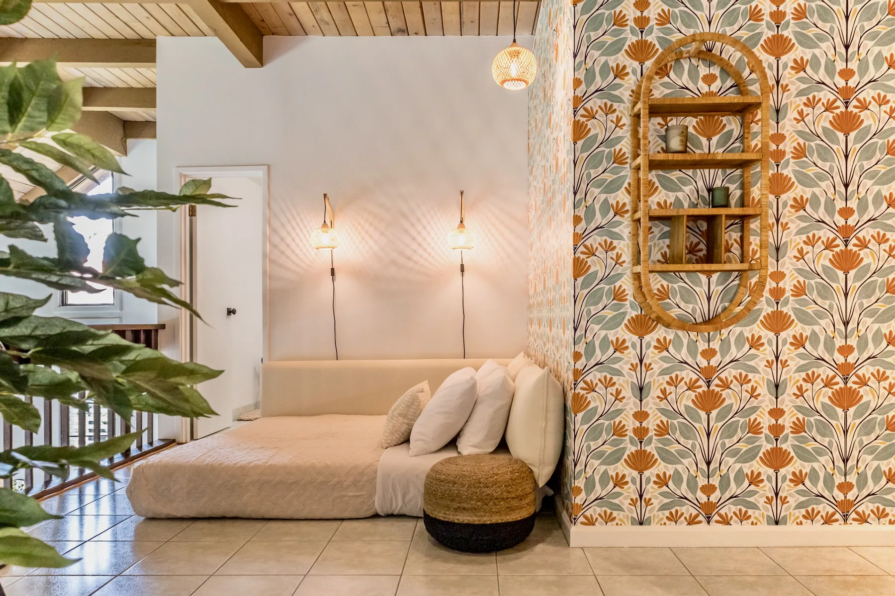 A bedroom with a low bed, leafy plant, and patterned wallpaper.