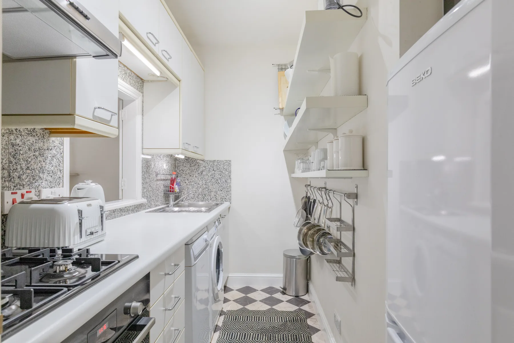A narrow kitchen with white cabinets, a countertop, and cooking appliances.