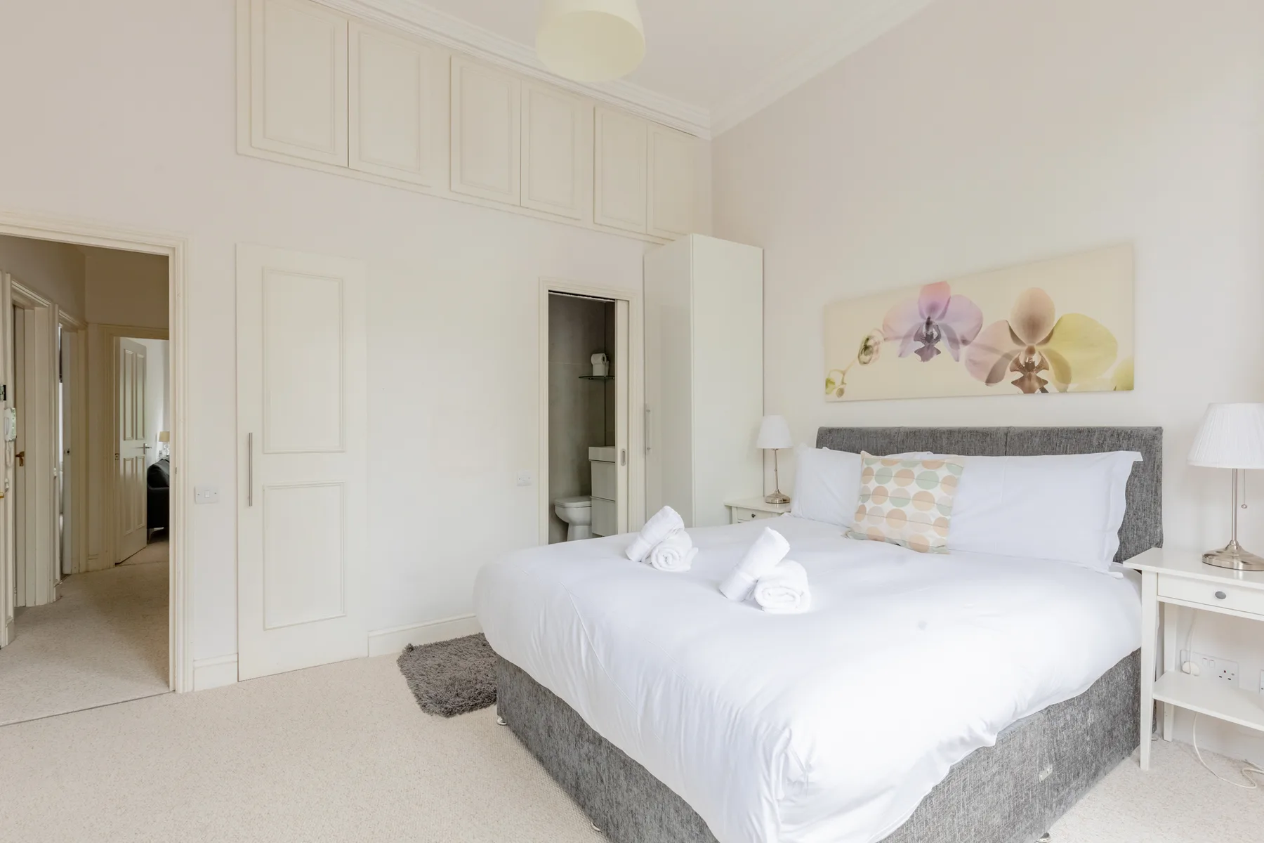 A bright bedroom with a large bed and floral artwork above the headboard.