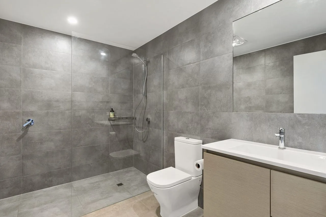 Un baño con azulejos, ducha, inodoro y un largo lavabo con encimera.