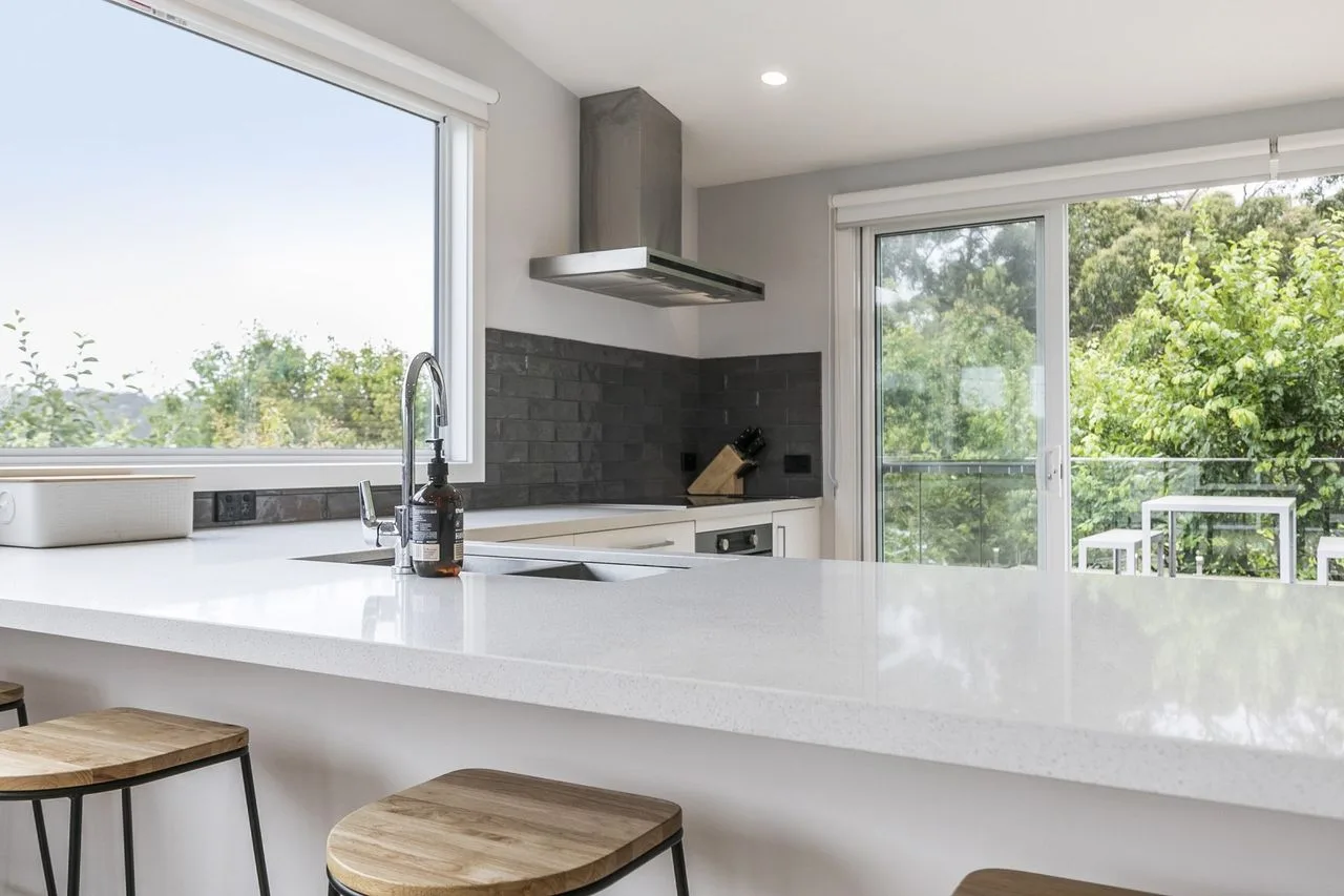 A bright kitchen with a wide island and glass doors opening to a leafy view.