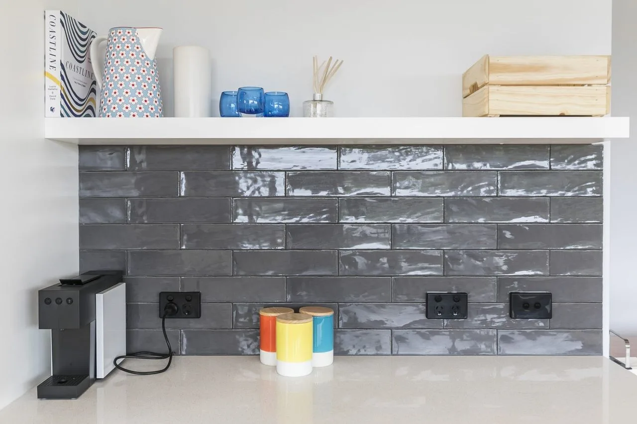 Una encimera de cocina con un microondas, recipientes coloridos y un salpicadero de azulejos oscuros.