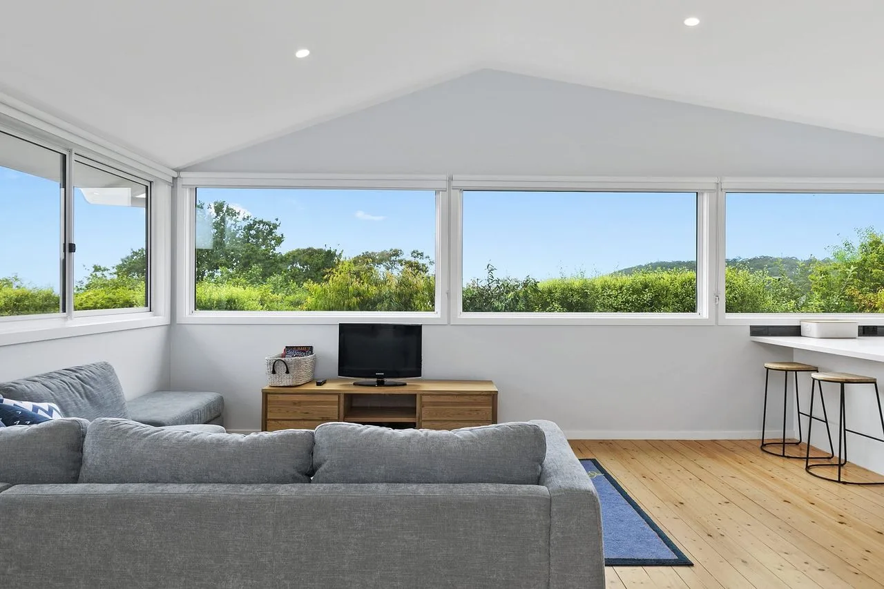 A bright living room with gray seating and wide windows overlooking greenery.