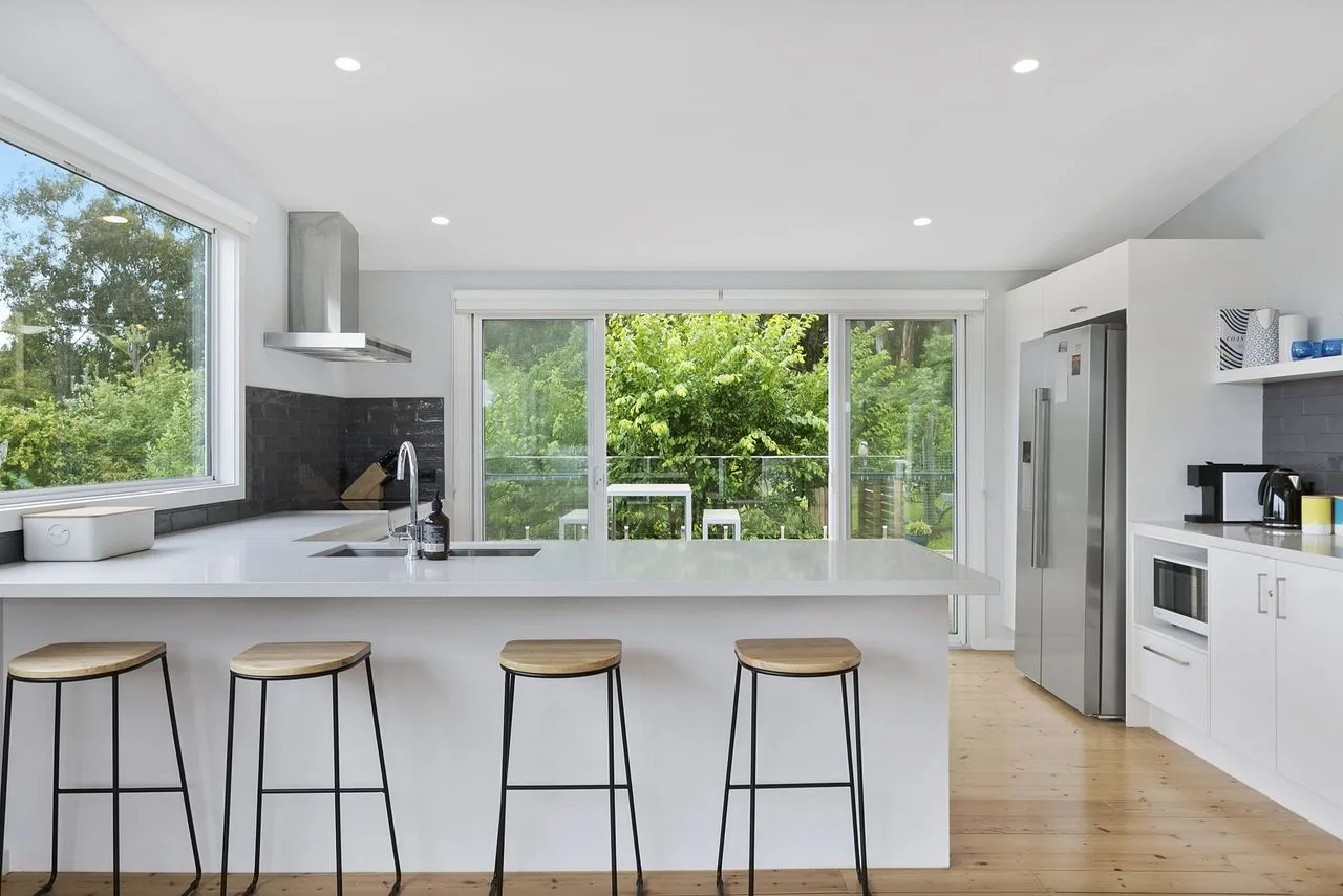 Una cocina luminosa con una isla amplia y grandes ventanas que dan a la vegetación.