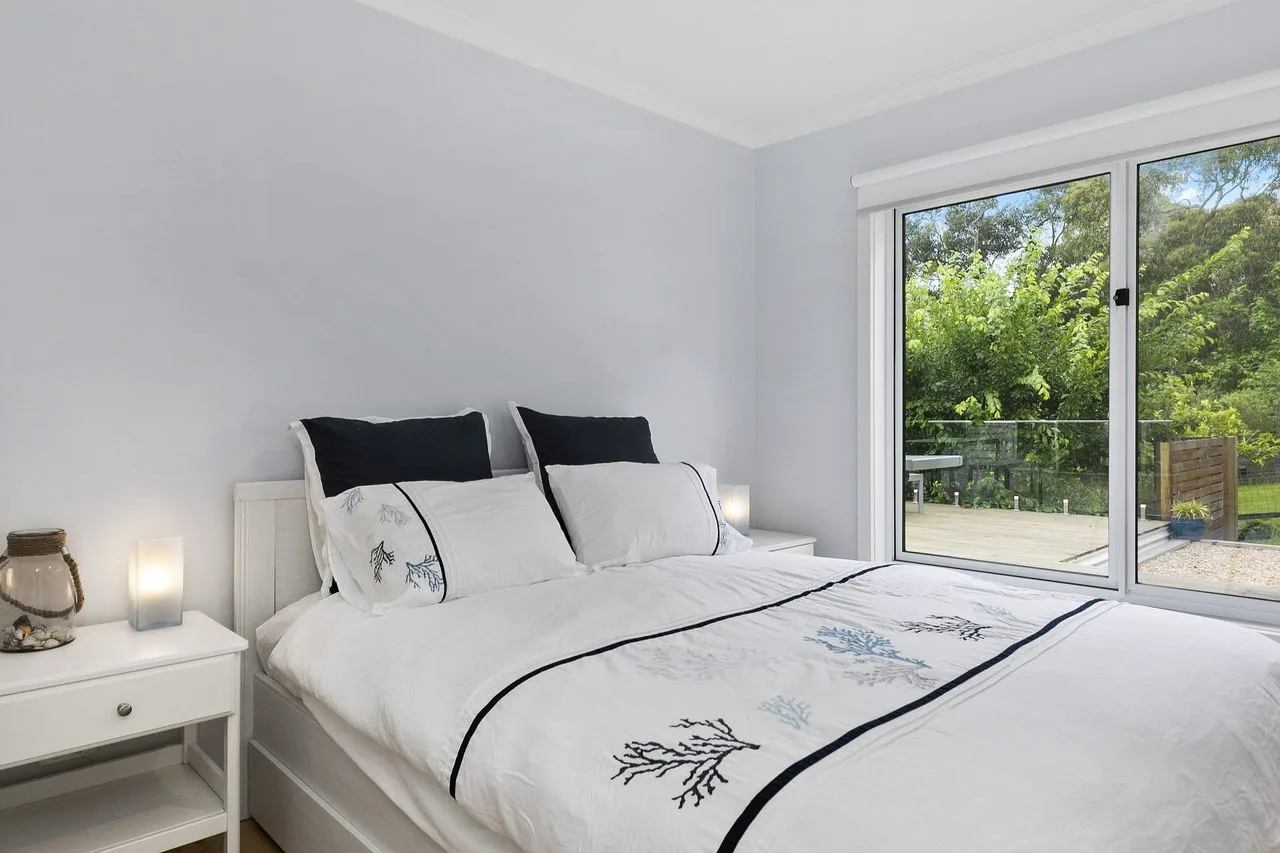 Un dormitorio luminoso con una cama tendida junto a una ventana grande.