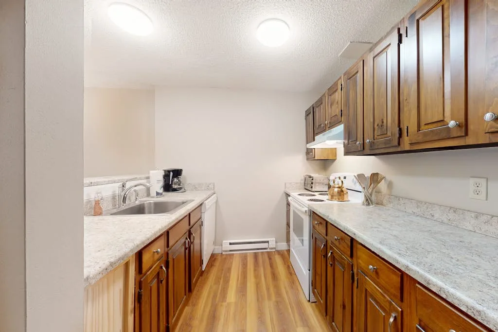 A narrow kitchen with wooden cabinets, countertops, and a stove.