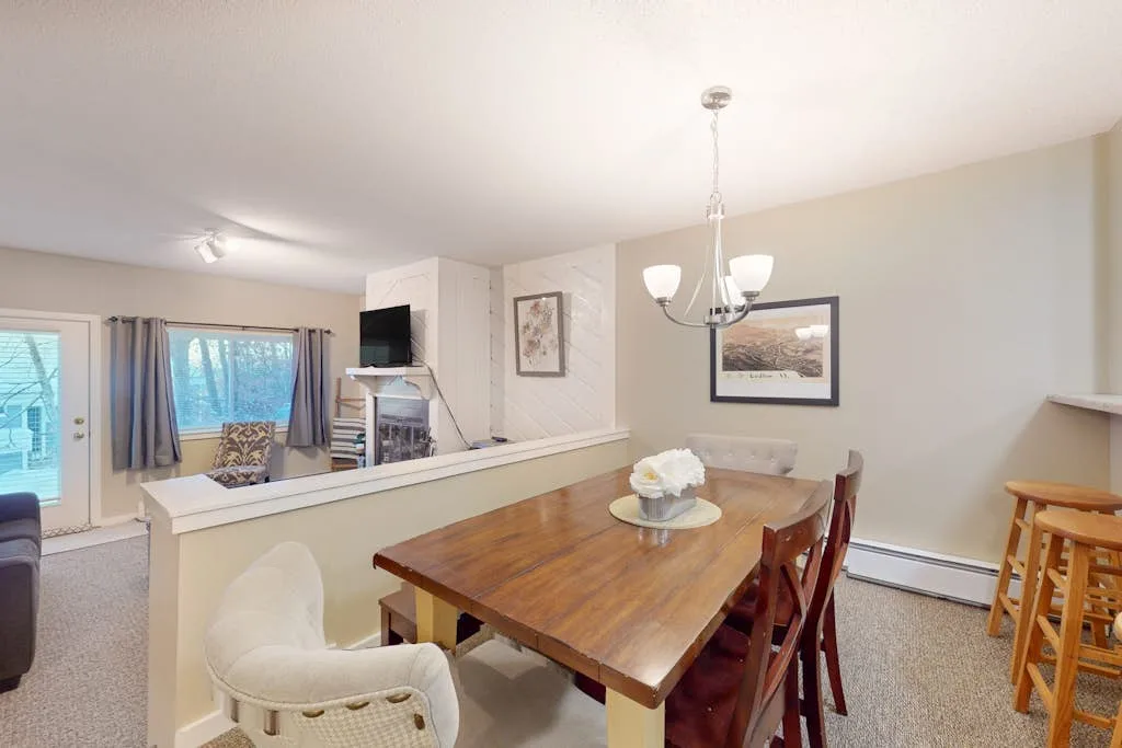 A dining area with a wooden table beside a raised counter and seating area.