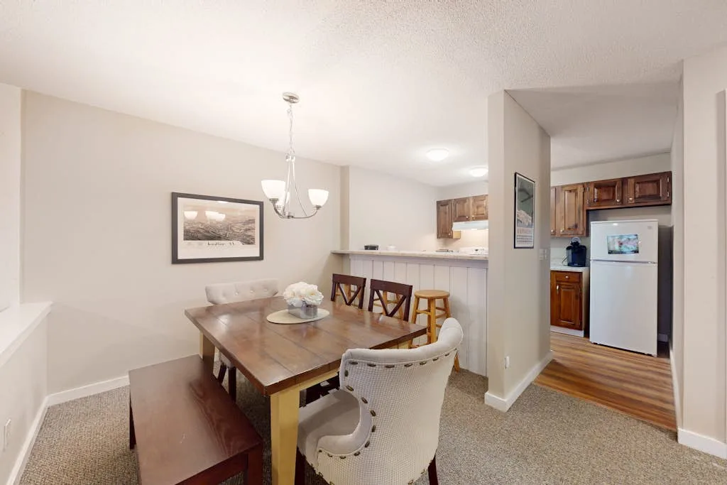A dining area with a wooden table and seating beside an open kitchen.