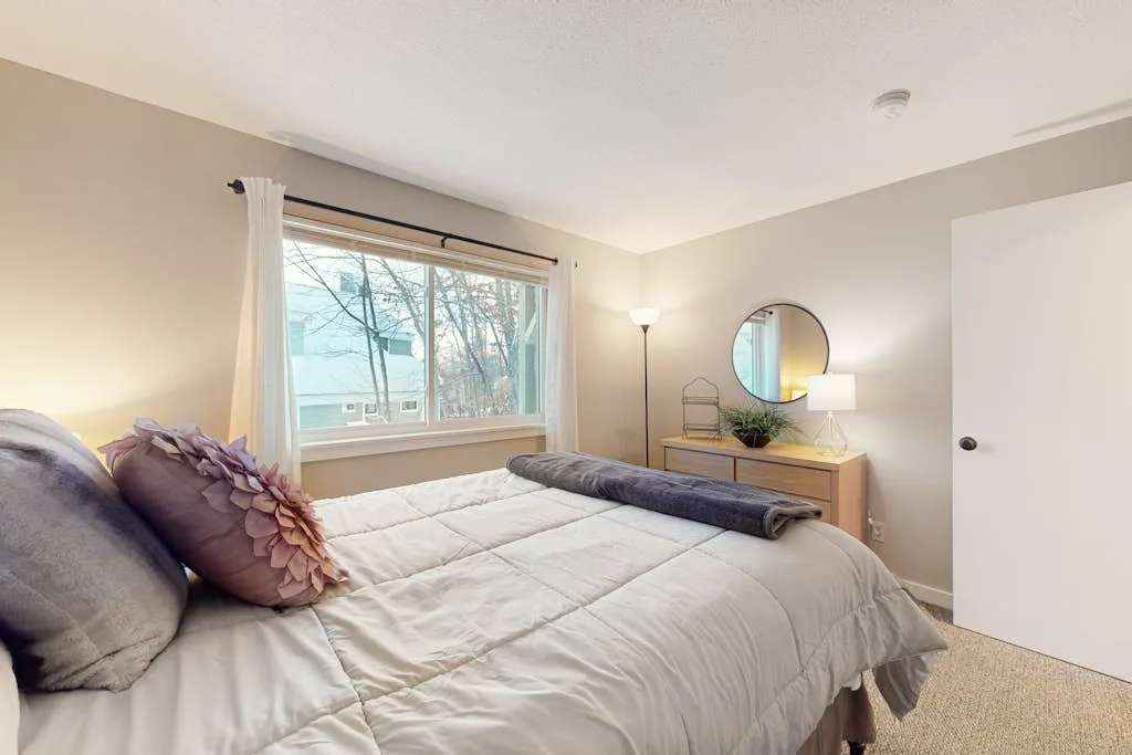 A bedroom with a bed, a dresser, and a round wall mirror.