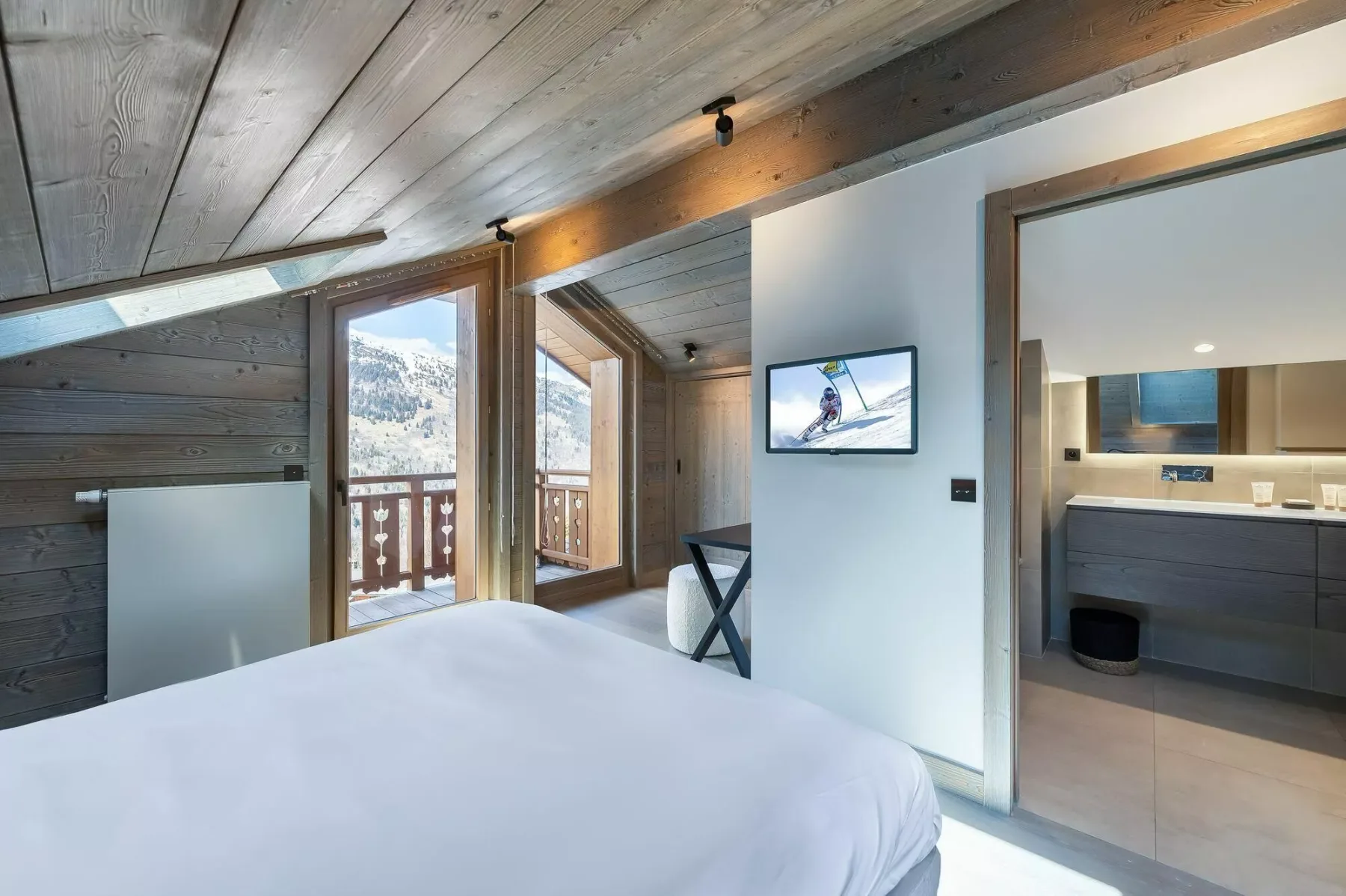 A bedroom with a bed, wall-mounted television, and an open doorway to a kitchenette.