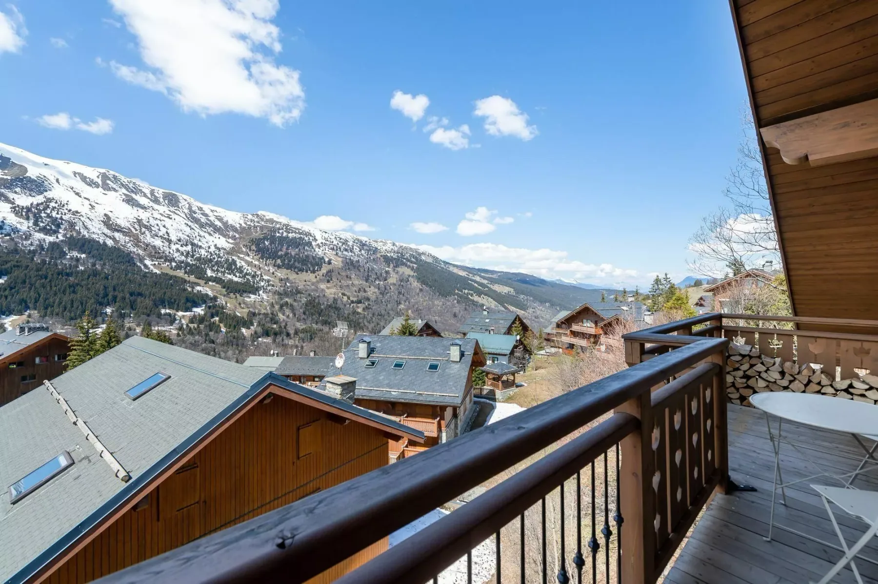A balcony overlooks chalet rooftops and a snow-dusted mountain range.