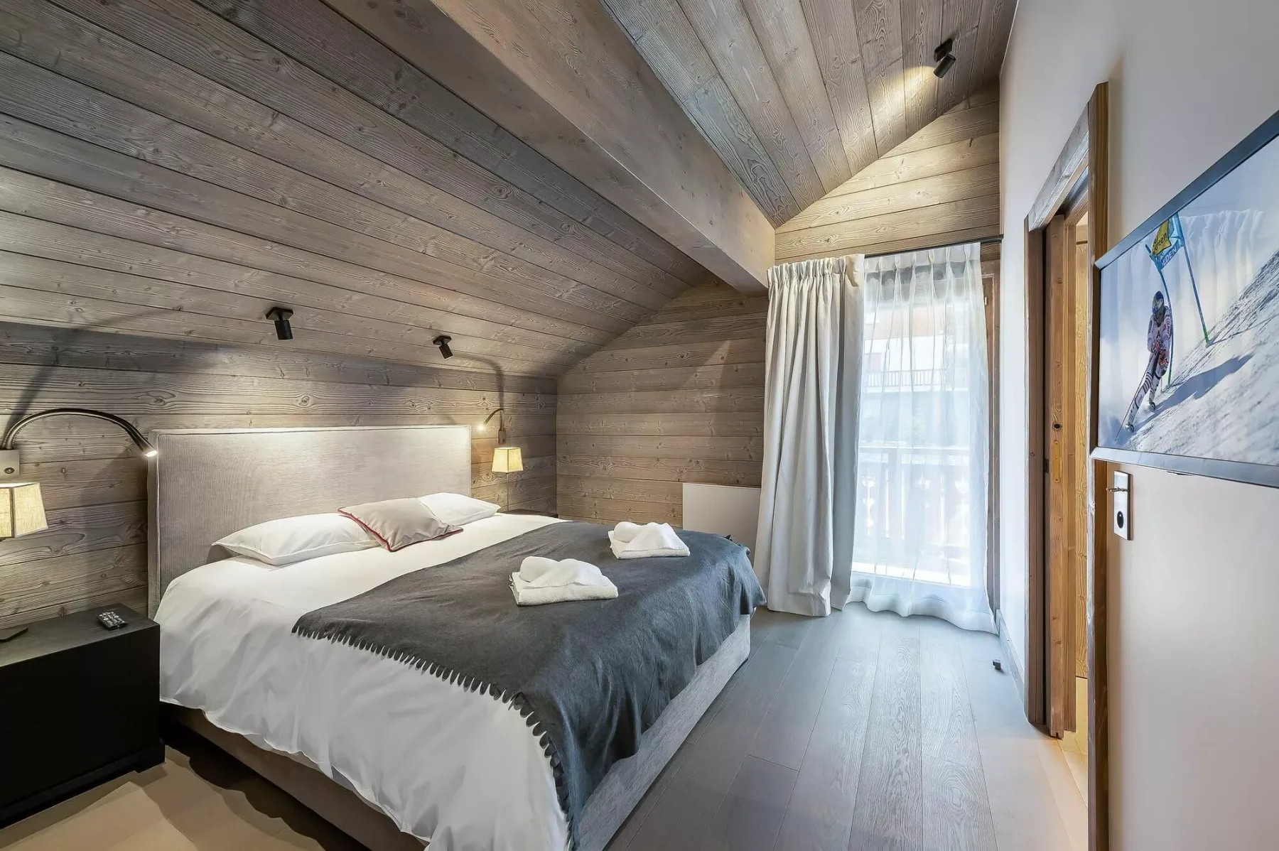 A bedroom with a double bed and a large curtained window.