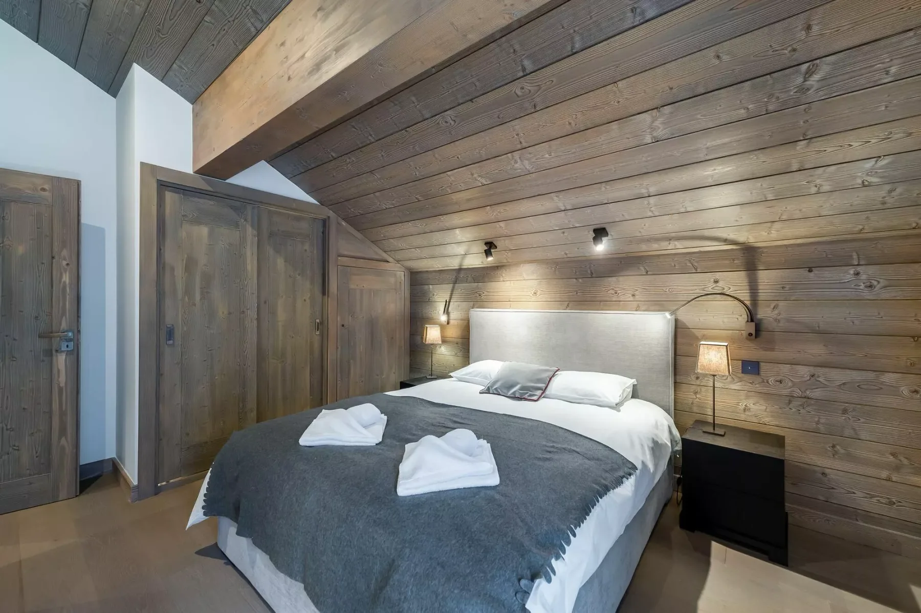 A bedroom with a bed, dark blanket, and wood-paneled walls.