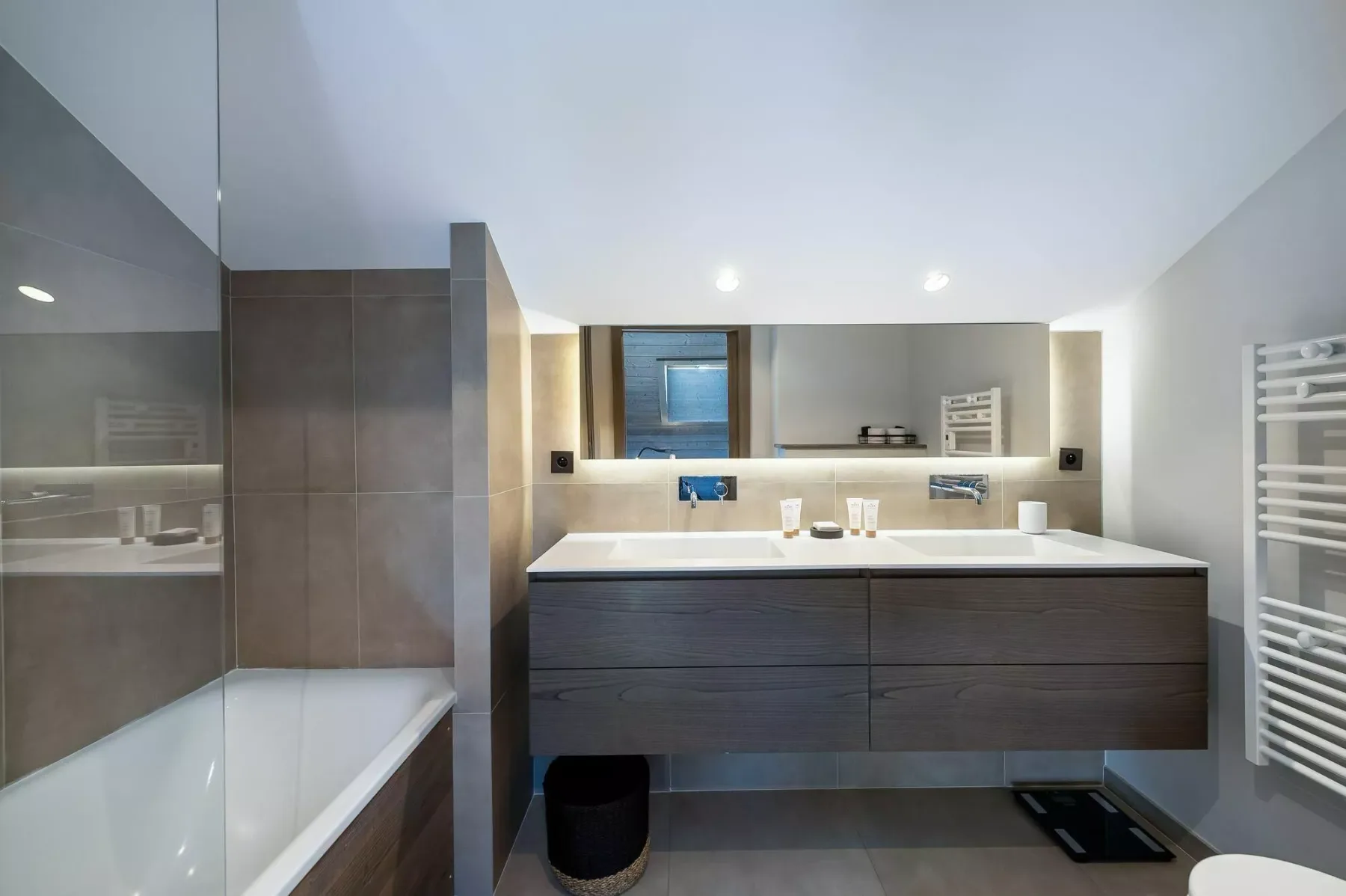 A modern bathroom with a bathtub, broad vanity, and wall-mounted towel warmer.