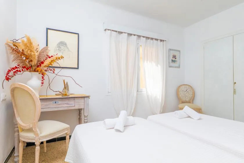 A bright bedroom with white bedding, a desk, and a curtained window.