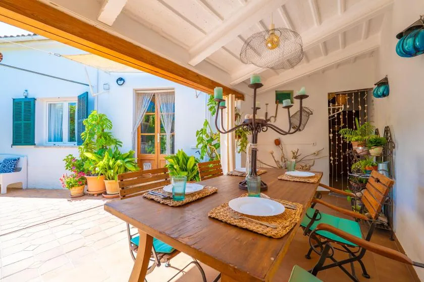 A covered patio dining area with a wooden table and surrounding plants.