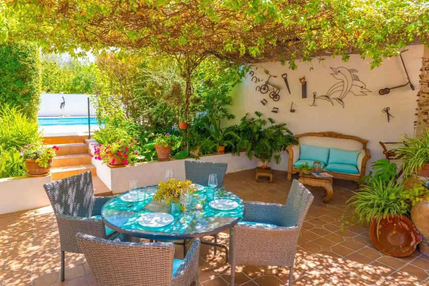 A leafy outdoor patio with a round dining table and cushioned seating.
