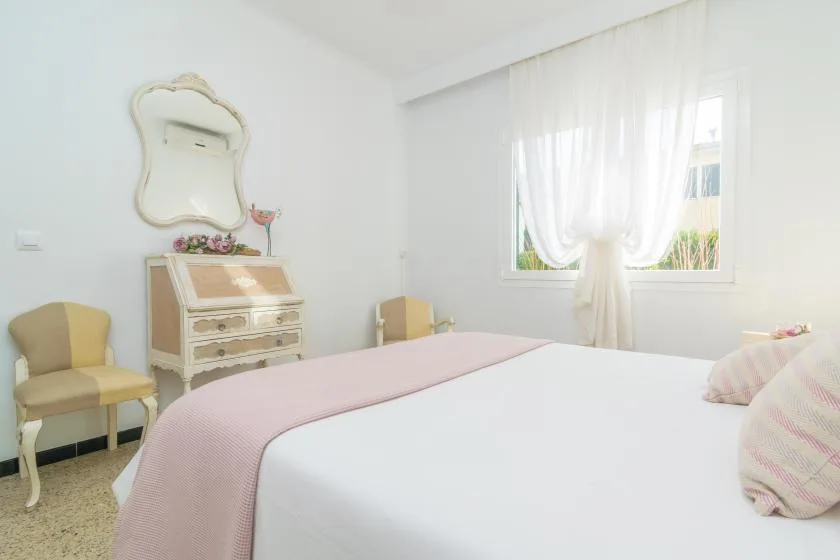 A bright bedroom with a bed, bedside seating, and sheer curtains.